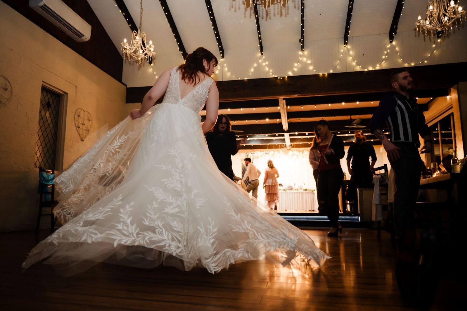 Wedding reception dance floor illuminated by warm chandelier light and string lights.