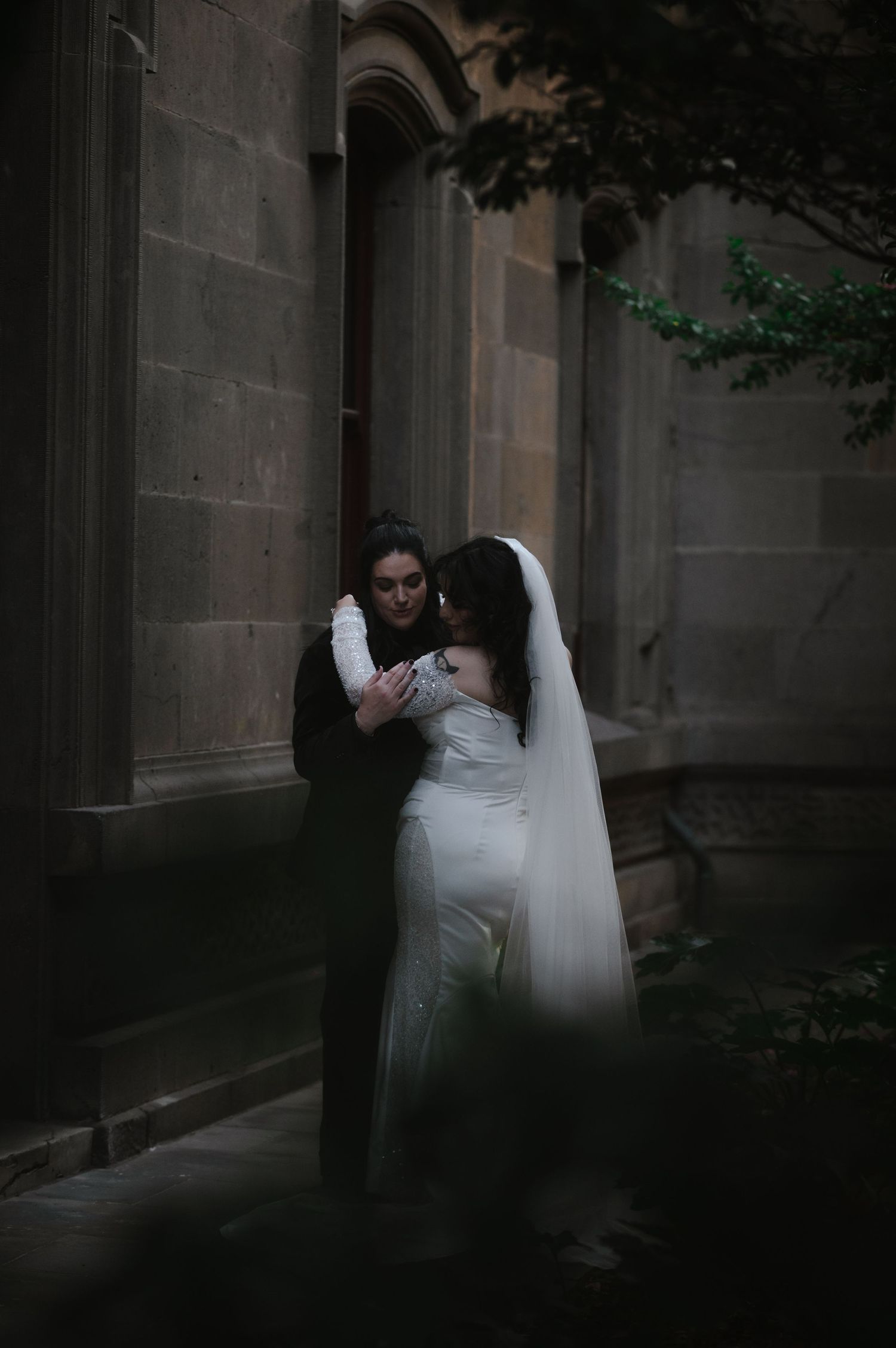 A moody wedding portrait against stone walls with dramatic shadows and lighting.