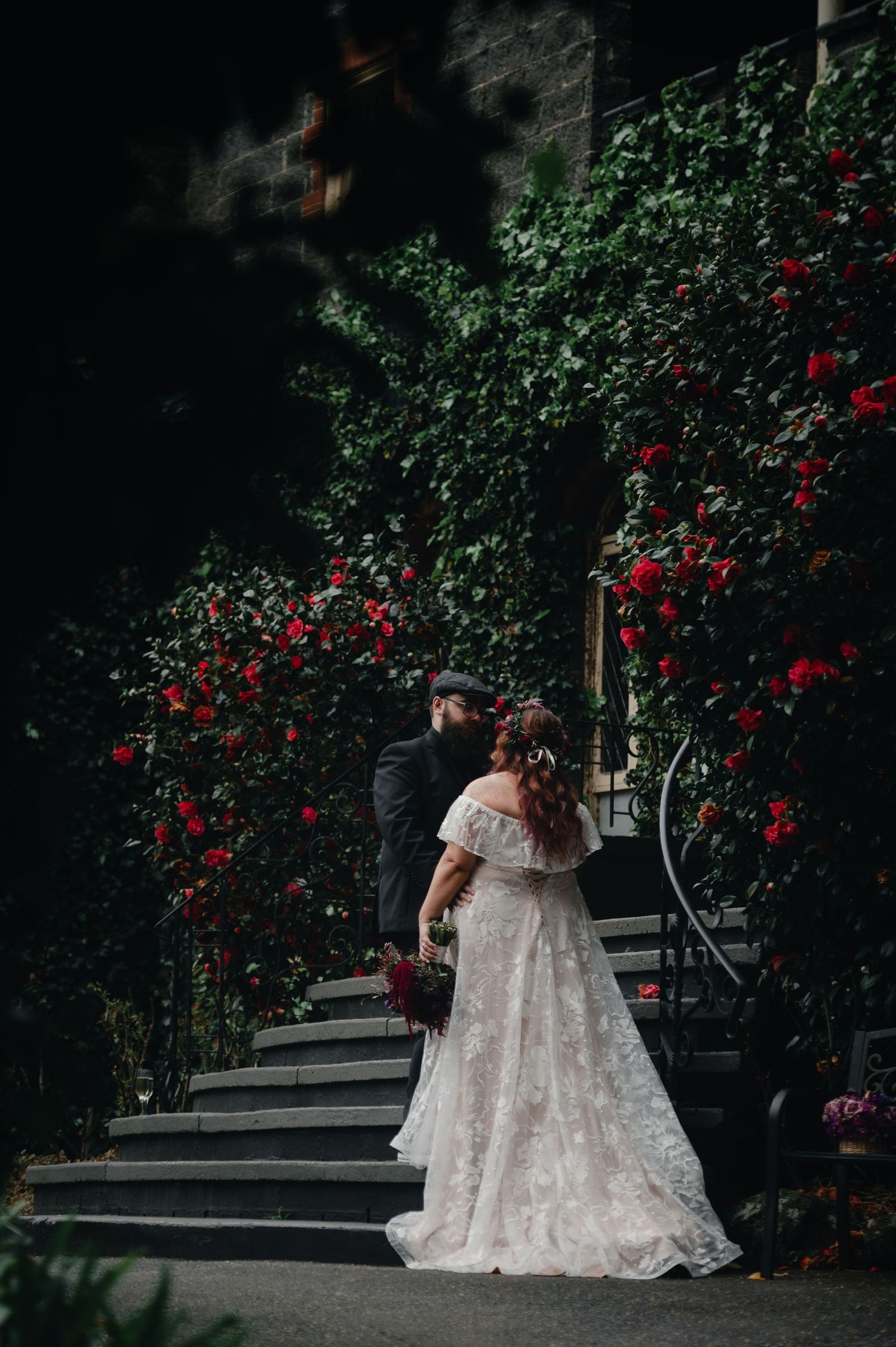 Wedding couple ascending stone steps amid climbing roses and ivy.