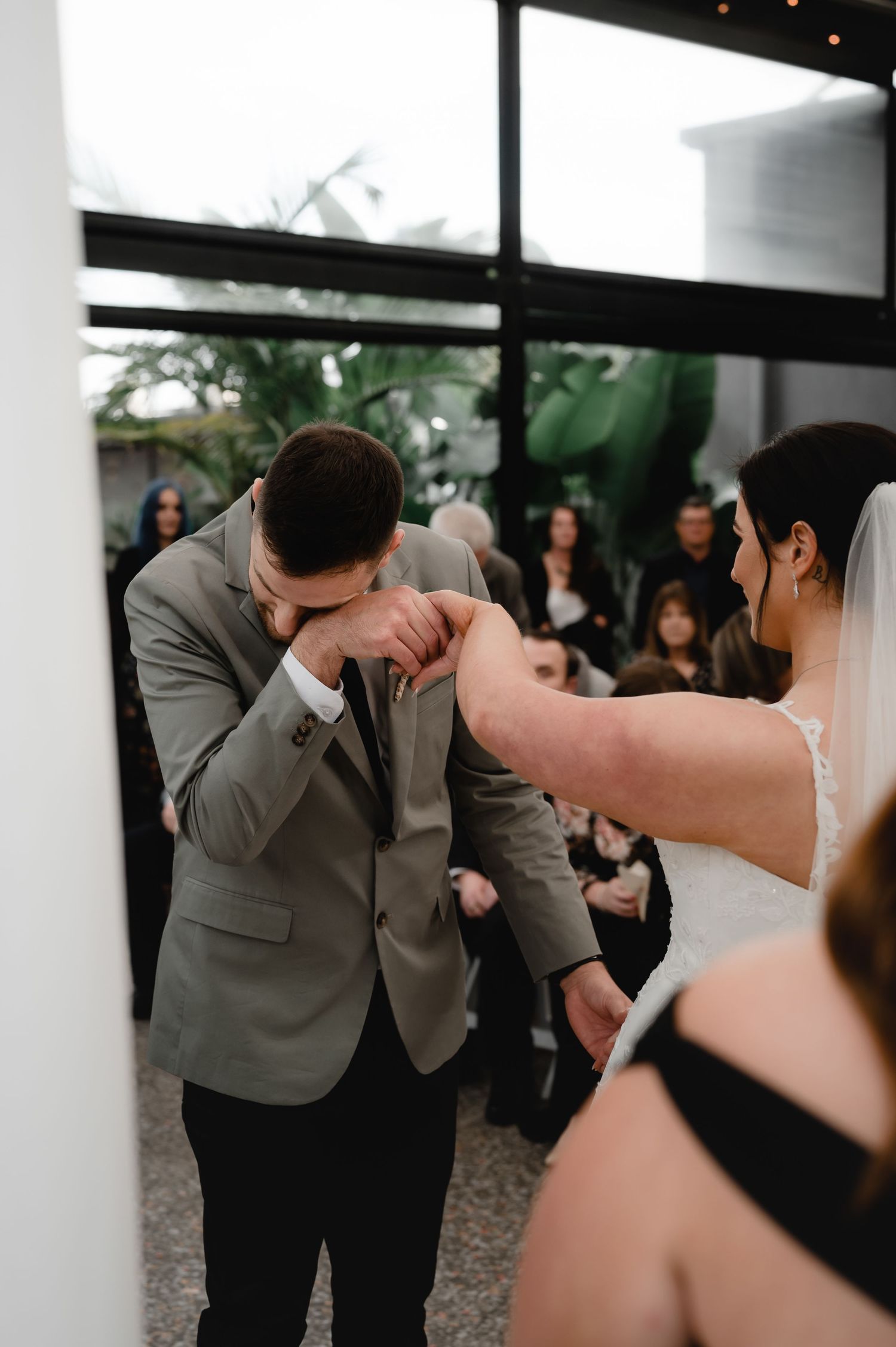 Candid wedding moment captured in a modern venue with large windows and natural lighting.