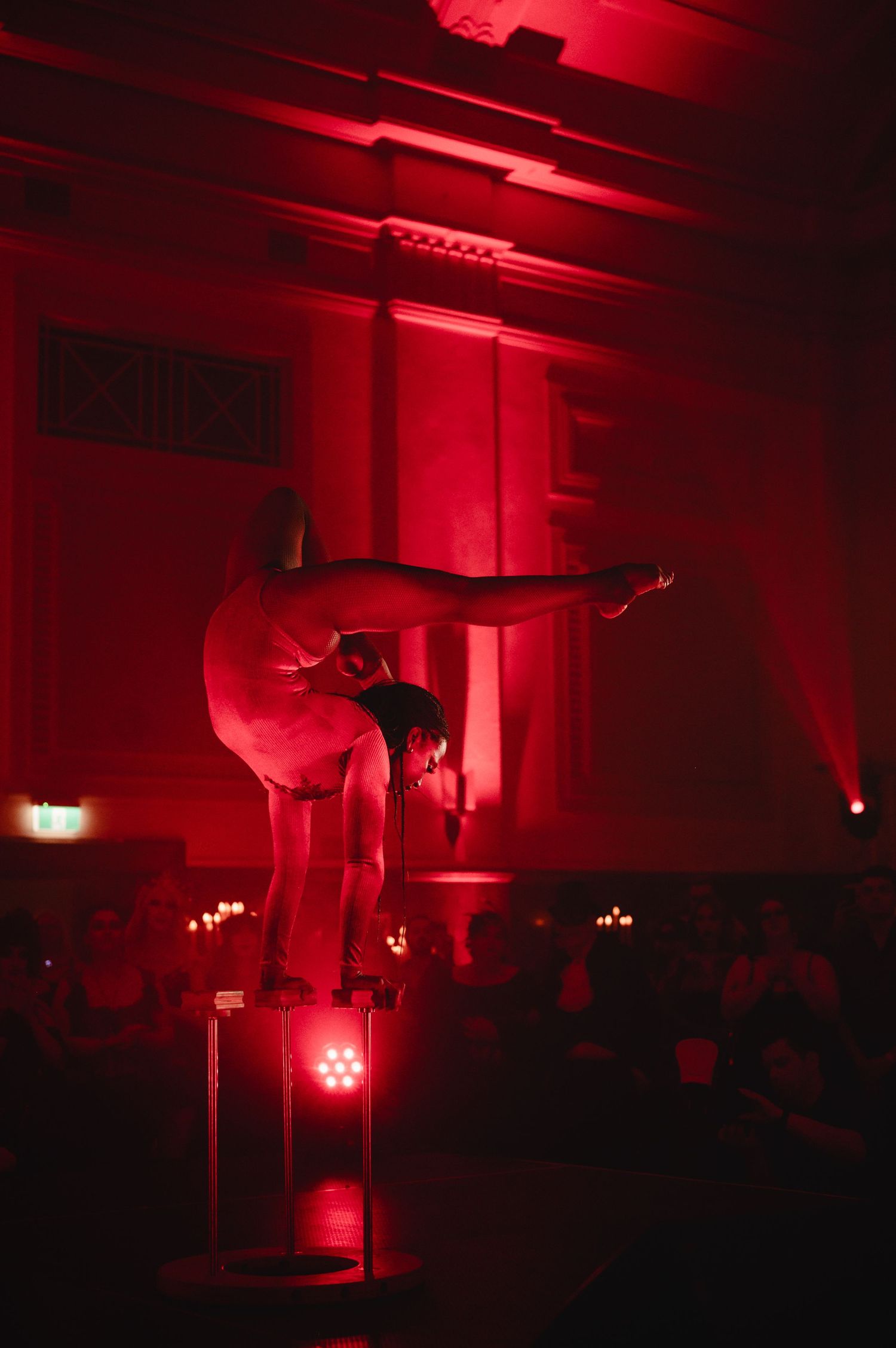 Dark room illuminated by dramatic red lighting creates an eerie atmosphere with silhouetted figures and equipment visible.