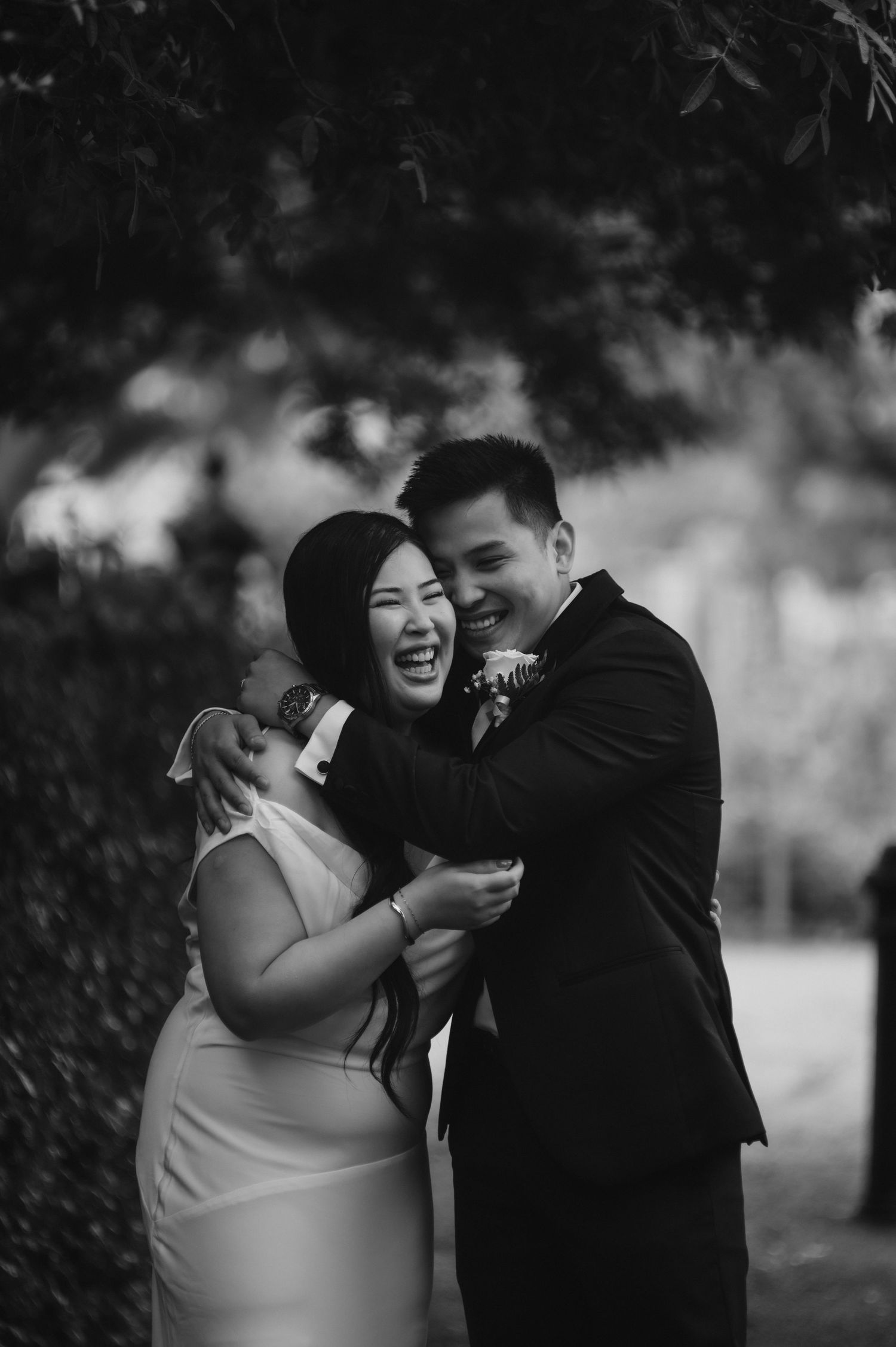 A couple shares a joyful candid moment together outdoors in black and white photography.