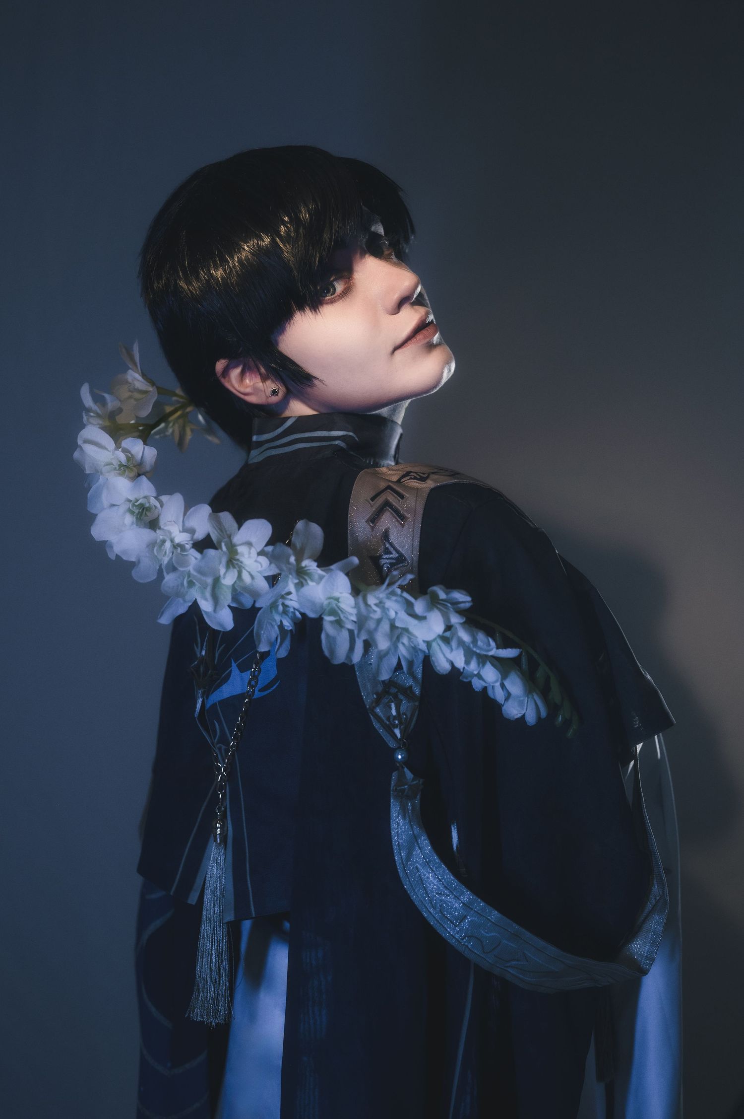 Stylized portrait with white orchids and dark clothing against moody backdrop.