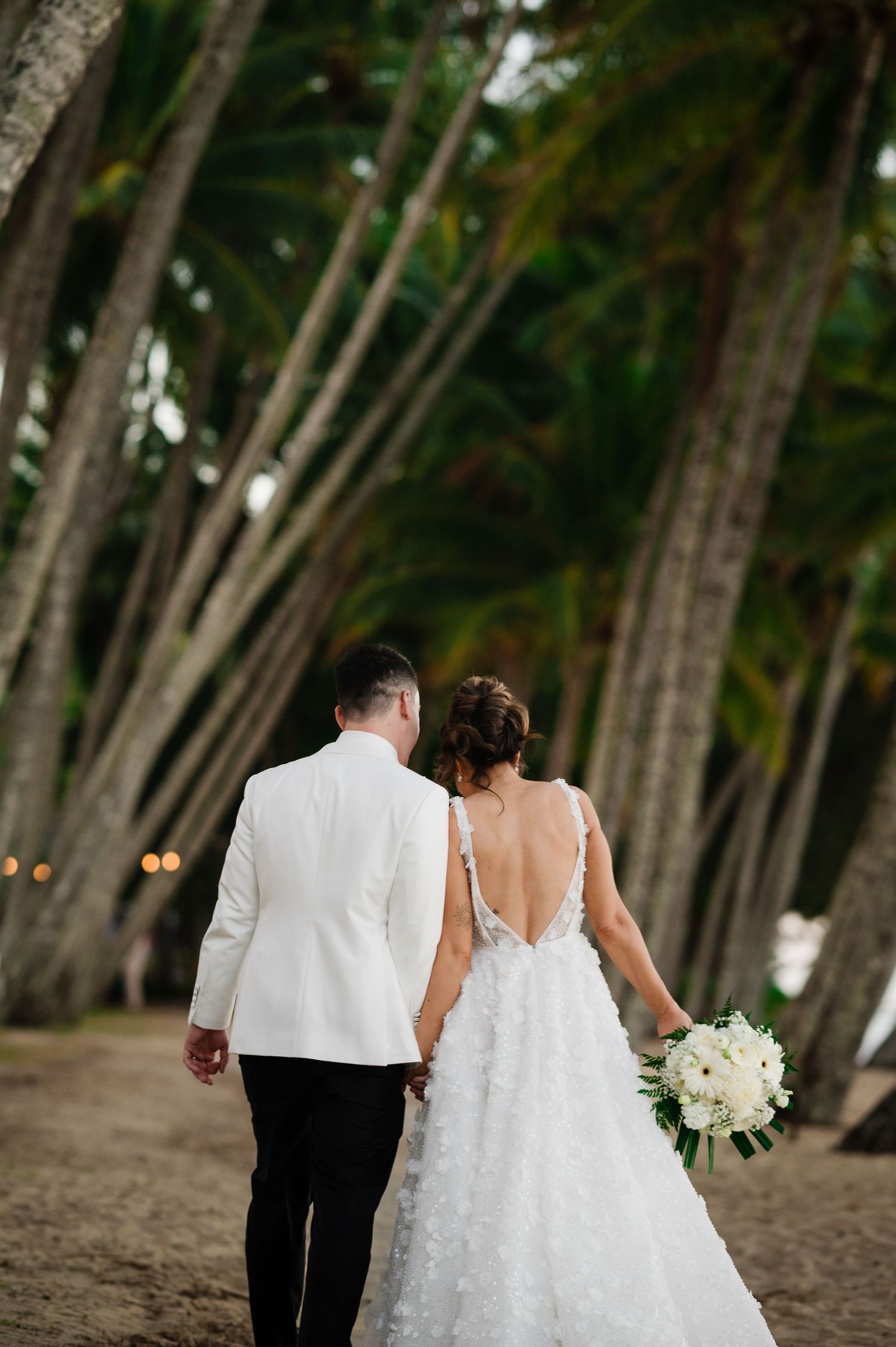Couple walks hand in hand through grove of tall trees during wedding portraits.