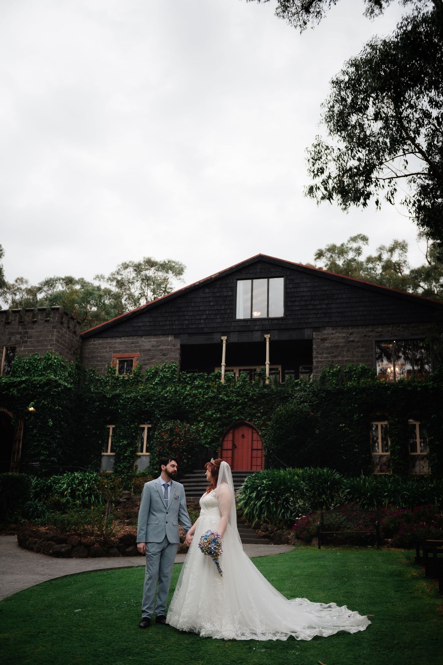 Newlyweds pose in front of rustic black barn with ivy-covered walls and manicured lawn.