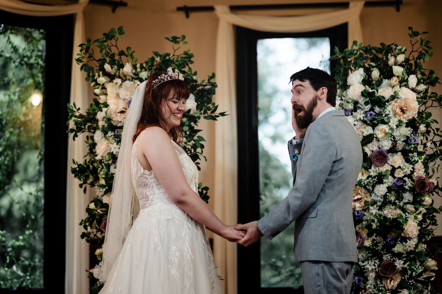 Wedding ceremony takes place under floral arch with white roses and greenery.