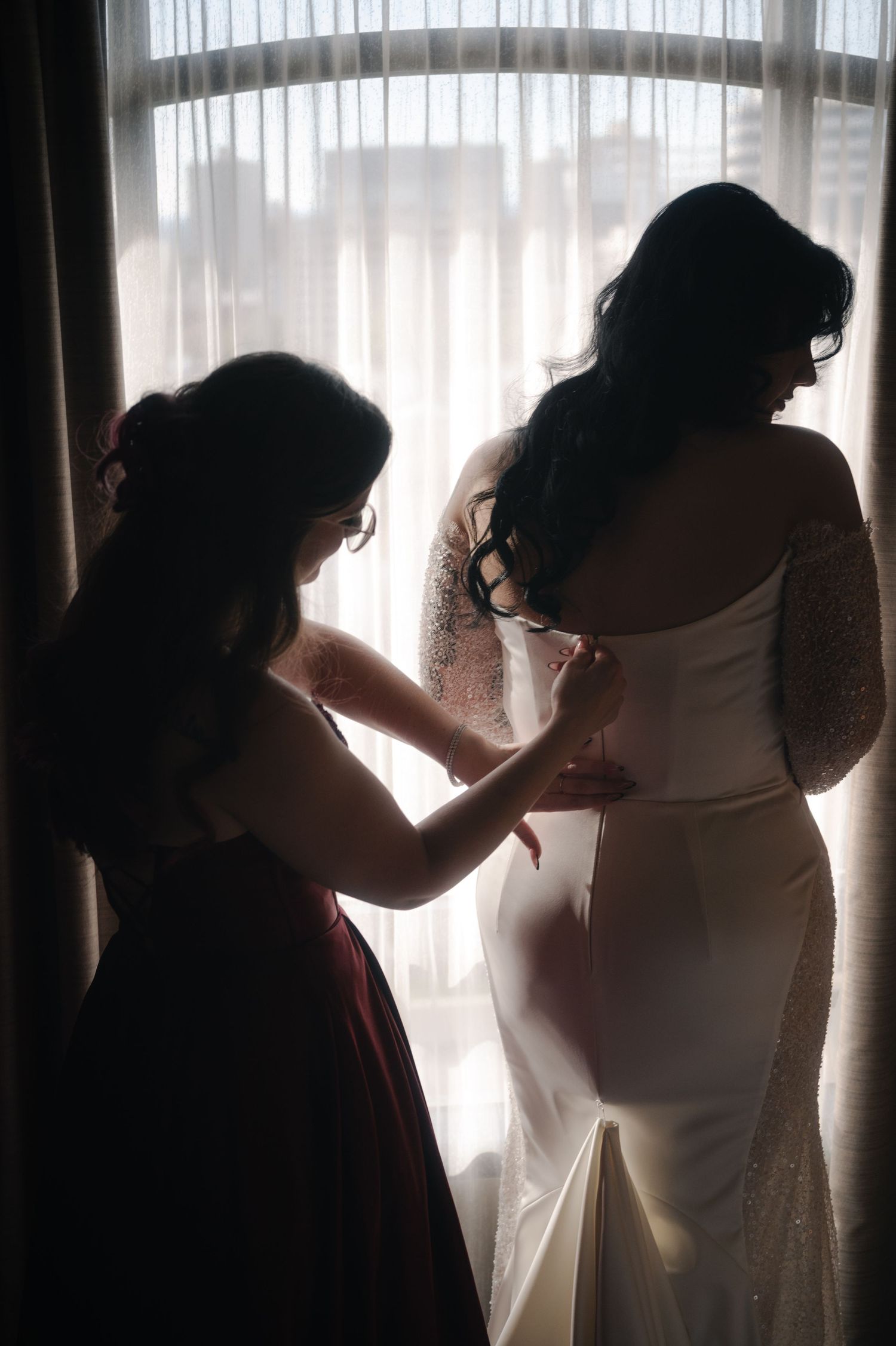 Backlit silhouettes against sheer curtains during a wedding preparation.