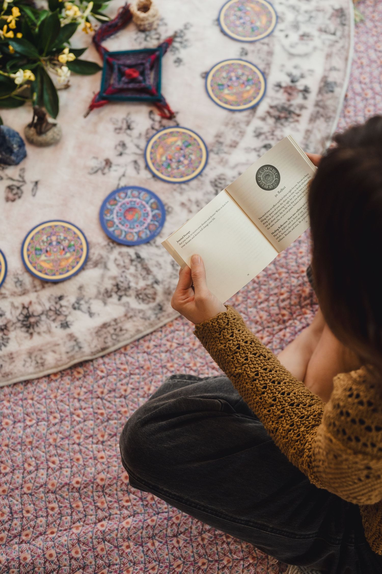 Person sitting cross-legged on a patterned rug, reading a book surrounded by decorative mandala tiles.