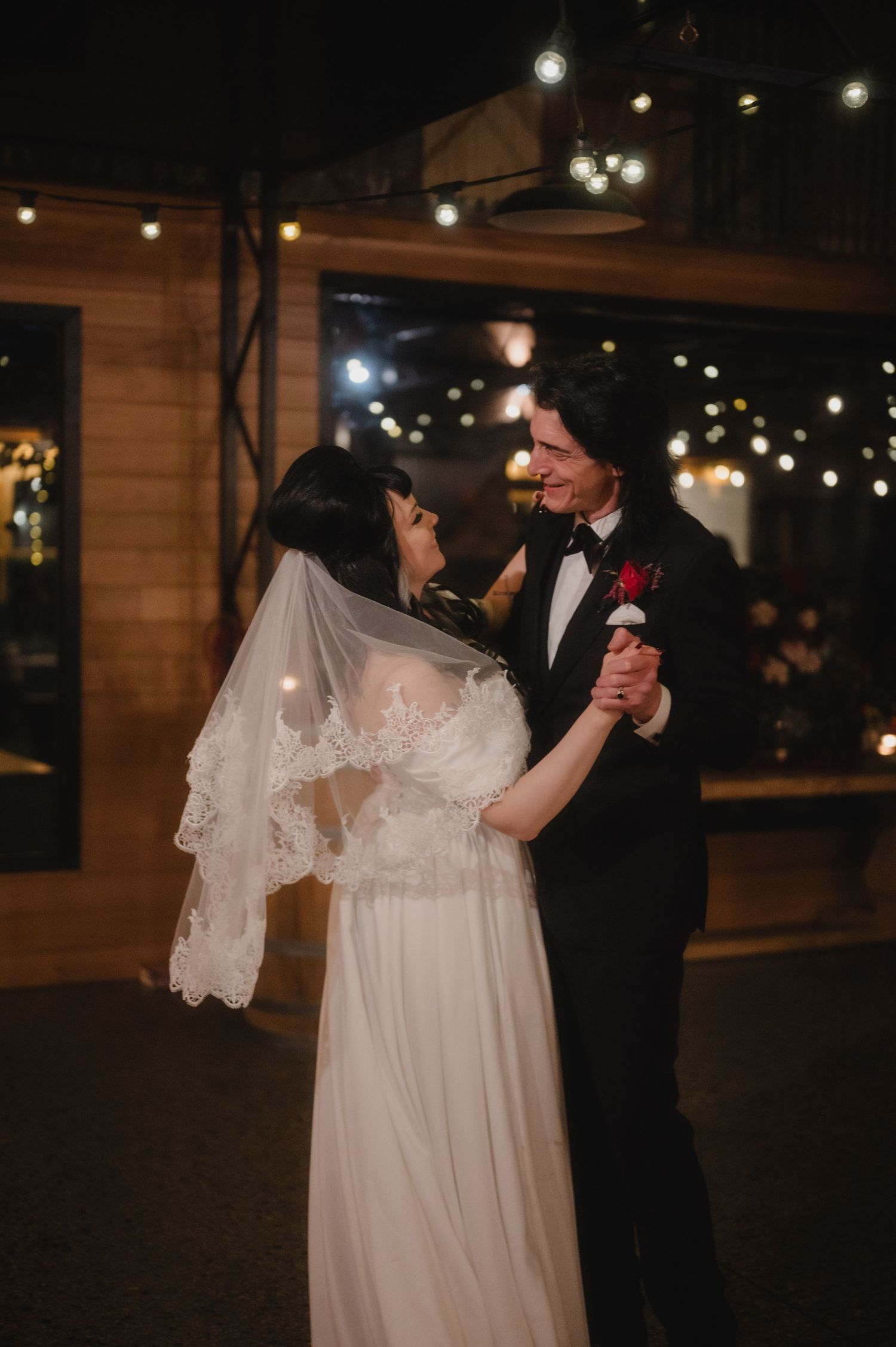 Couple dancing together under twinkling string lights at an evening outdoor wedding reception.