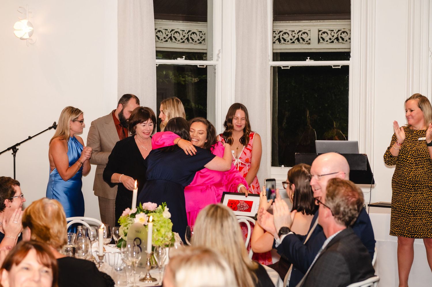 A large group of people gathered at a formal dinner party in an elegant white room with tables and chairs.