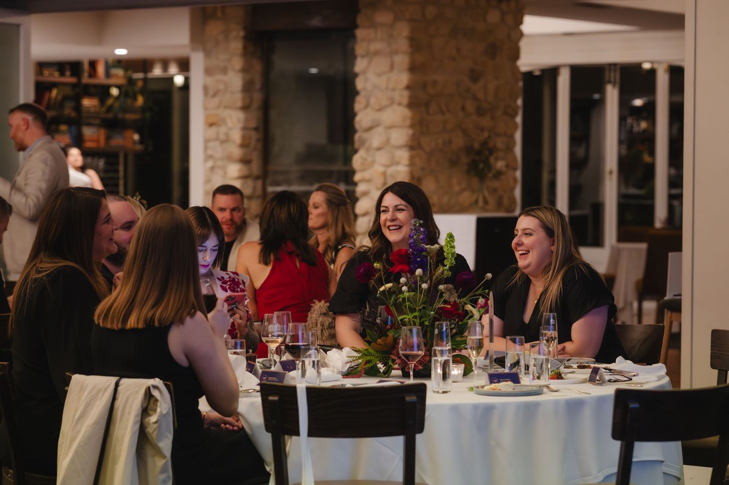 Dinner guests enjoying conversation and wine at elegant tables with stone columns in a restaurant setting.