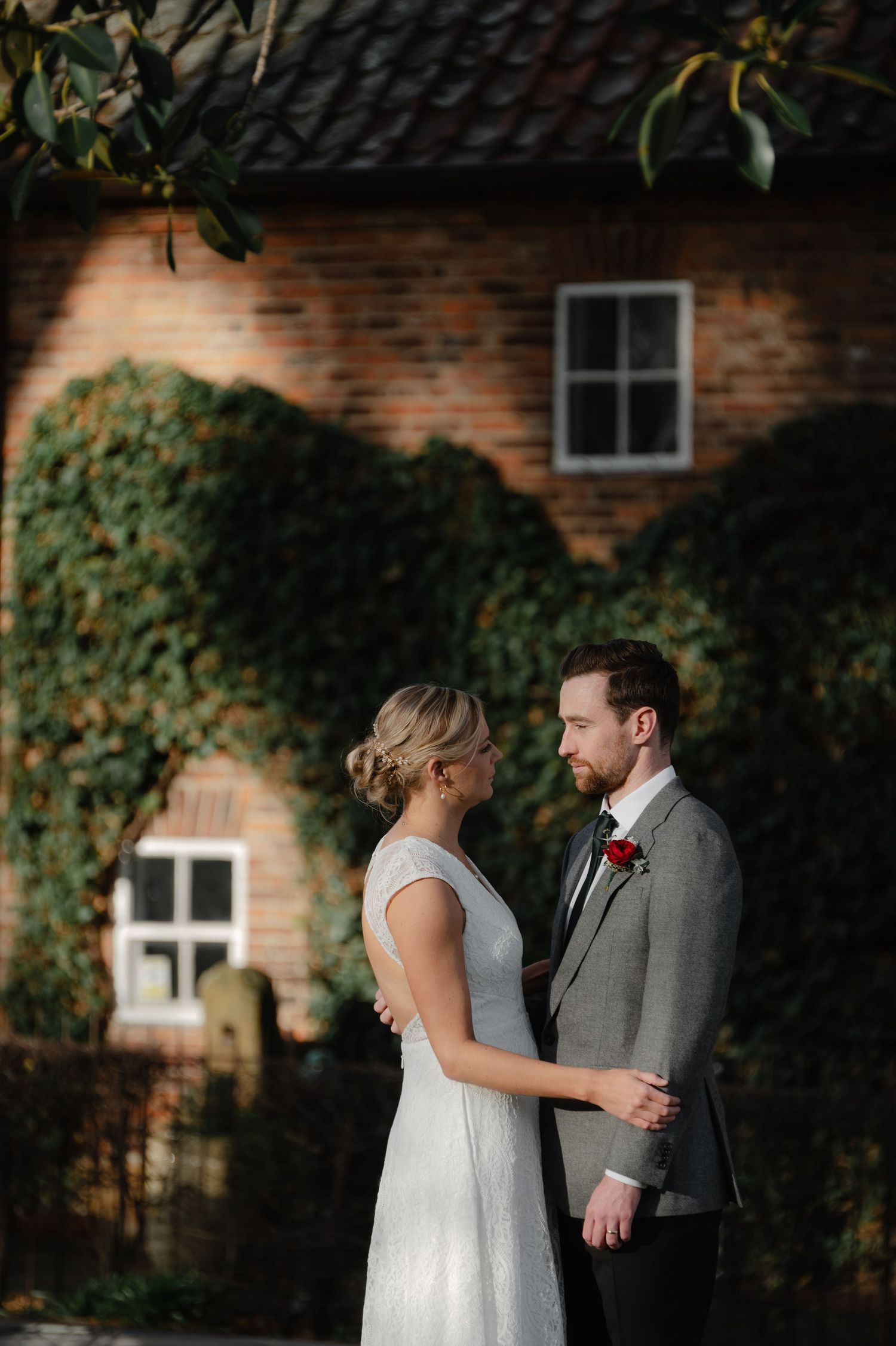 Couple shares romantic moment against brick wall with climbing ivy.
