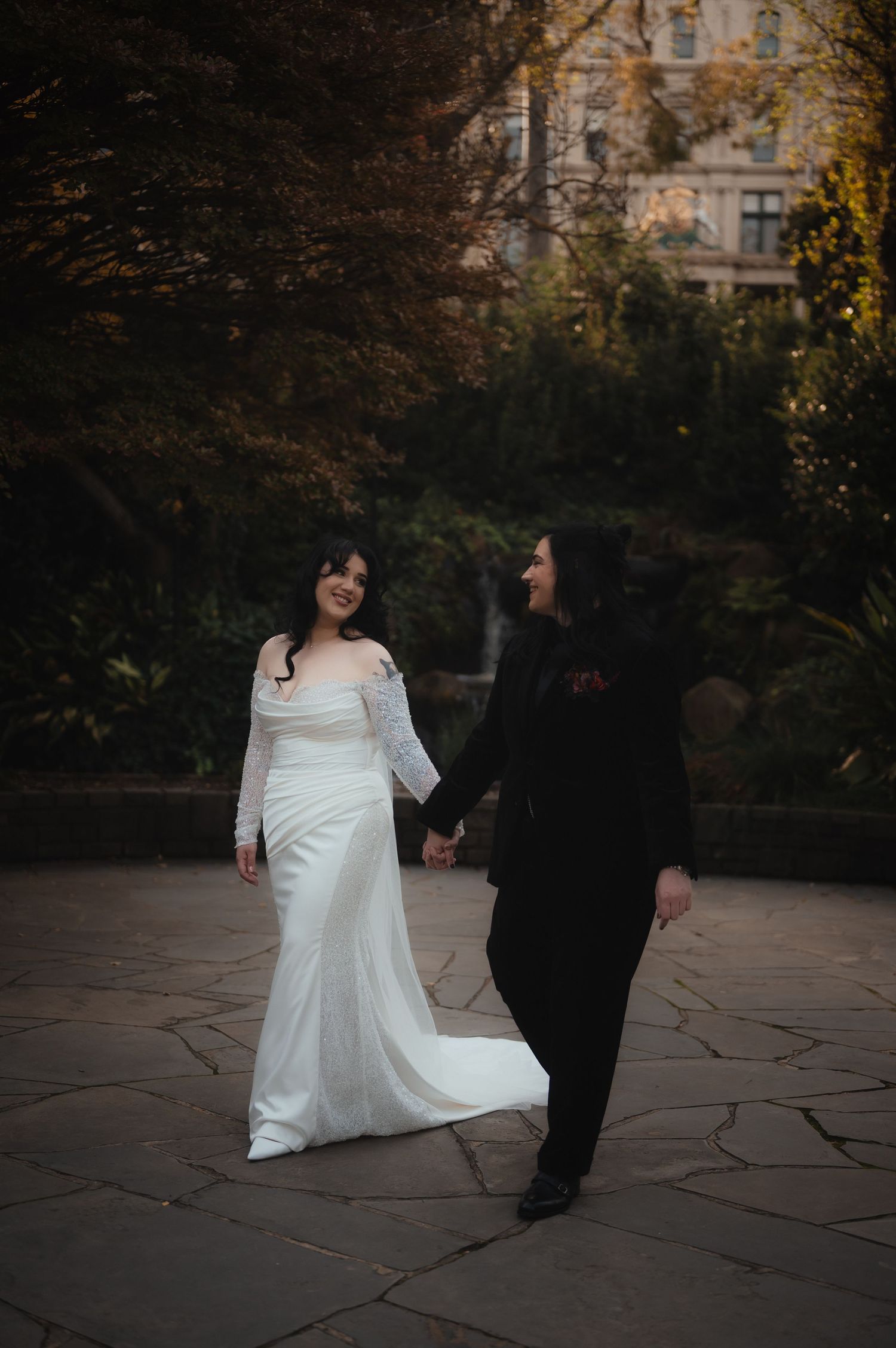 Wedding couple walking on stone patio surrounded by autumn foliage.