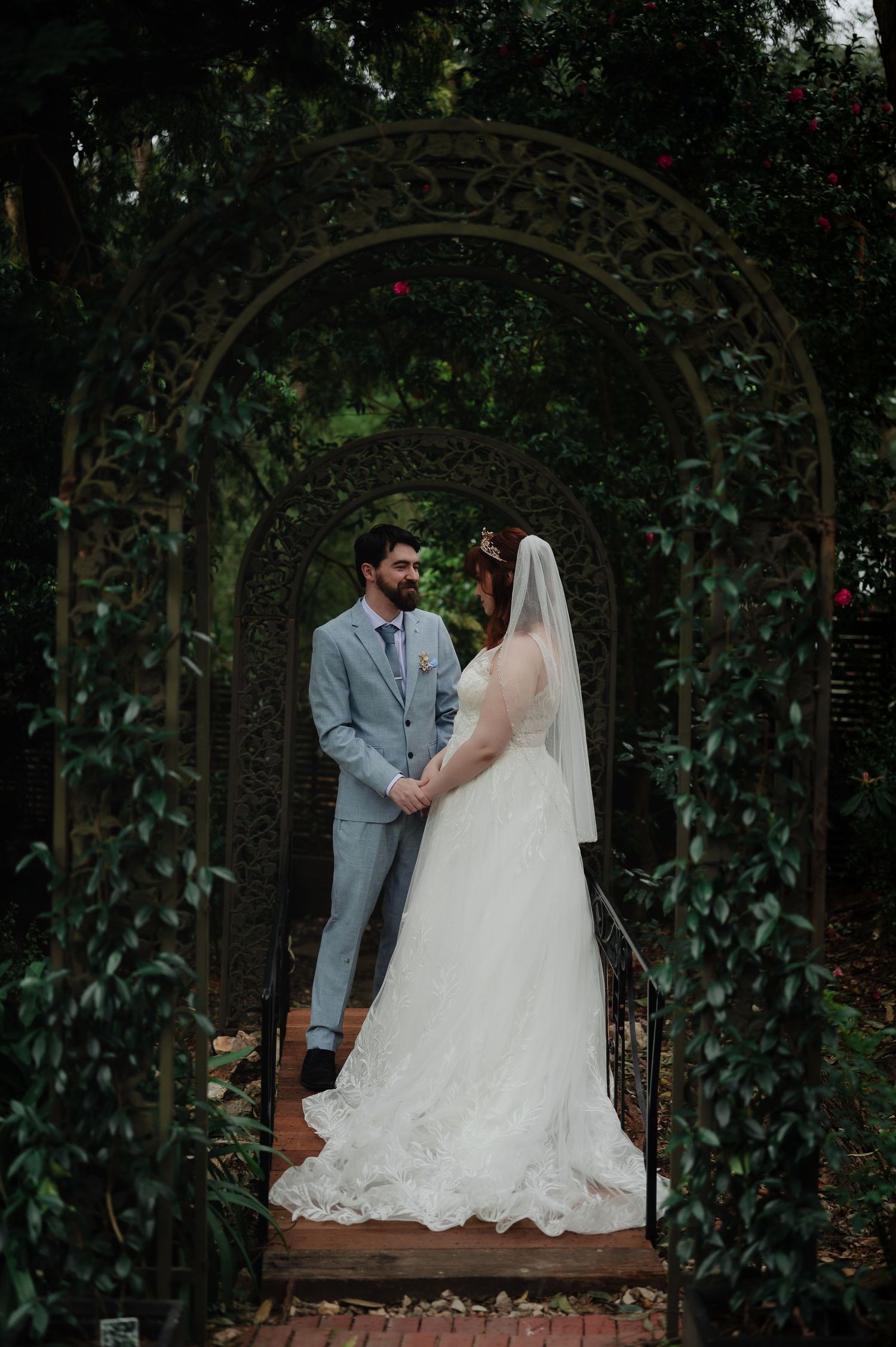 Couple shares intimate moment under garden arbor decorated with climbing vines.