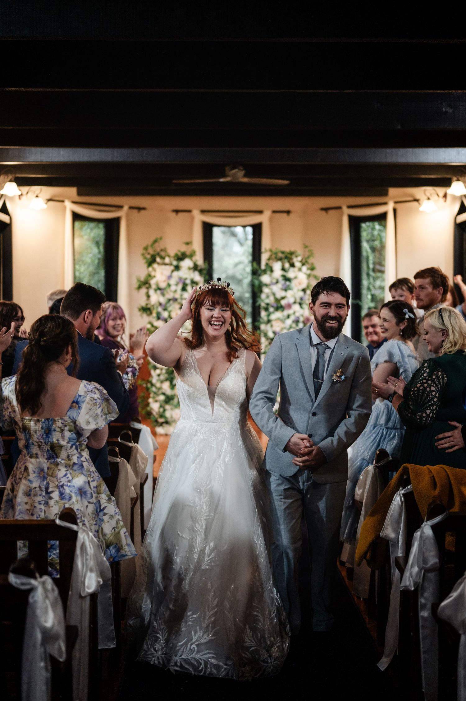 Wedding celebration with guests and couple in dimly lit venue with floral decorations.