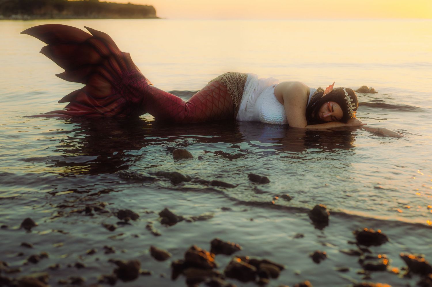 Artistic beach photography with figure reclining in shallow water at sunset.