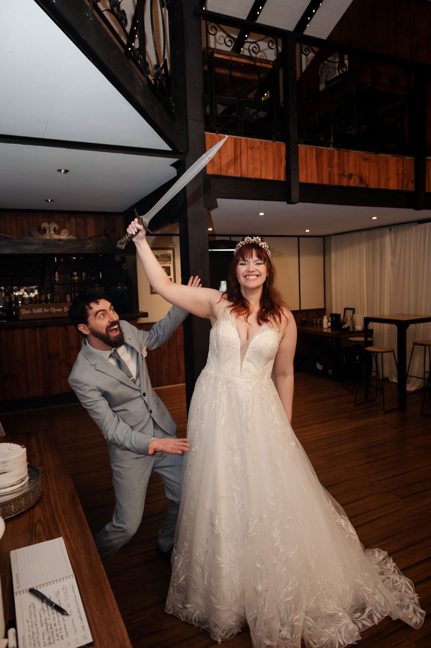 Newlyweds share a fun dance moment on a hardwood floor with elegant lighting overhead.