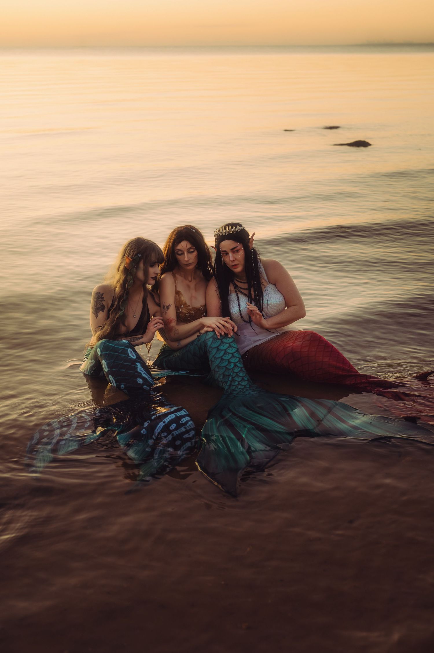Group wearing mermaid costumes pose together on beach at sunset.