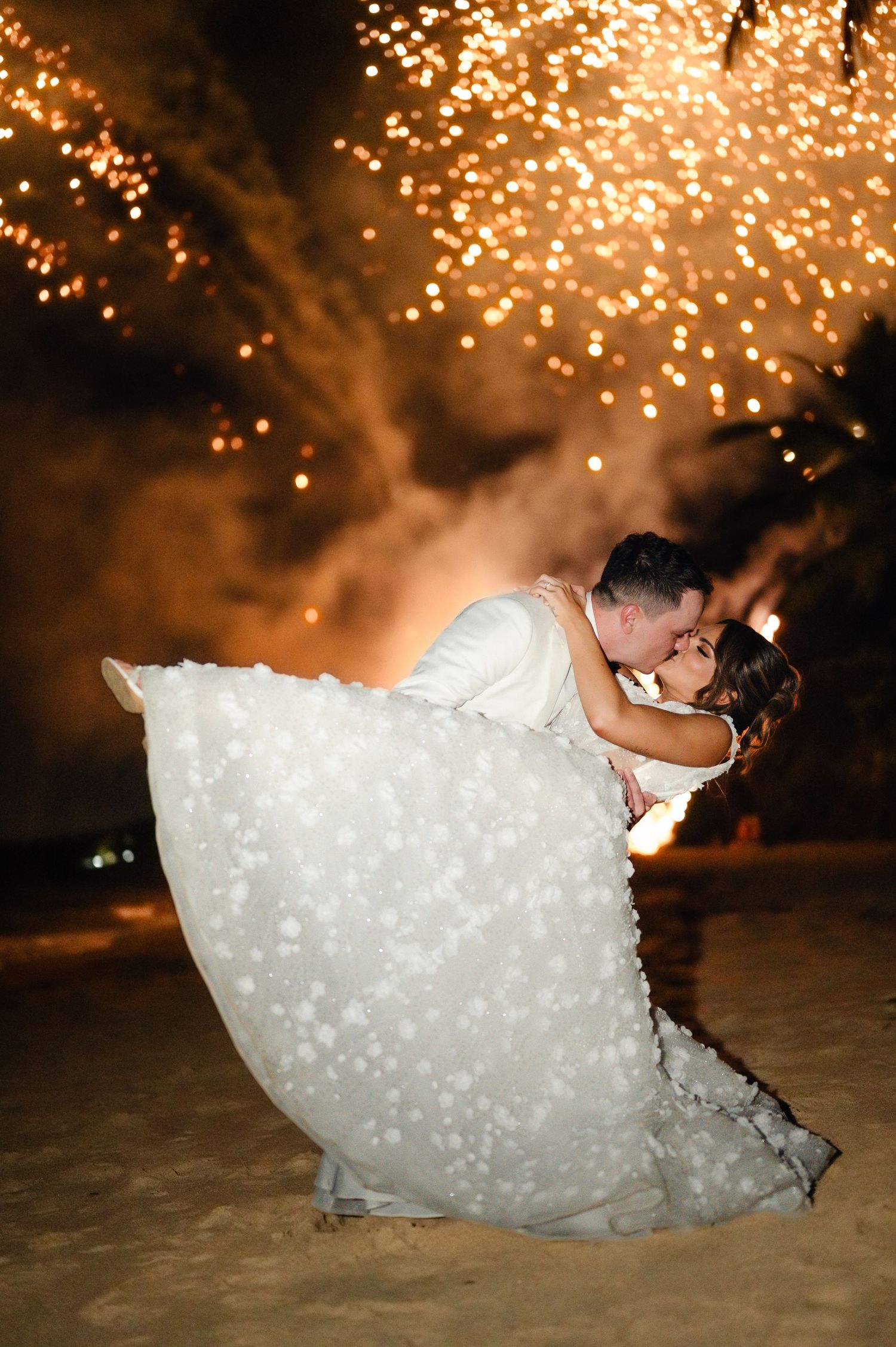 Dramatic dip kiss on the beach with sparkling lights creating a magical backdrop.