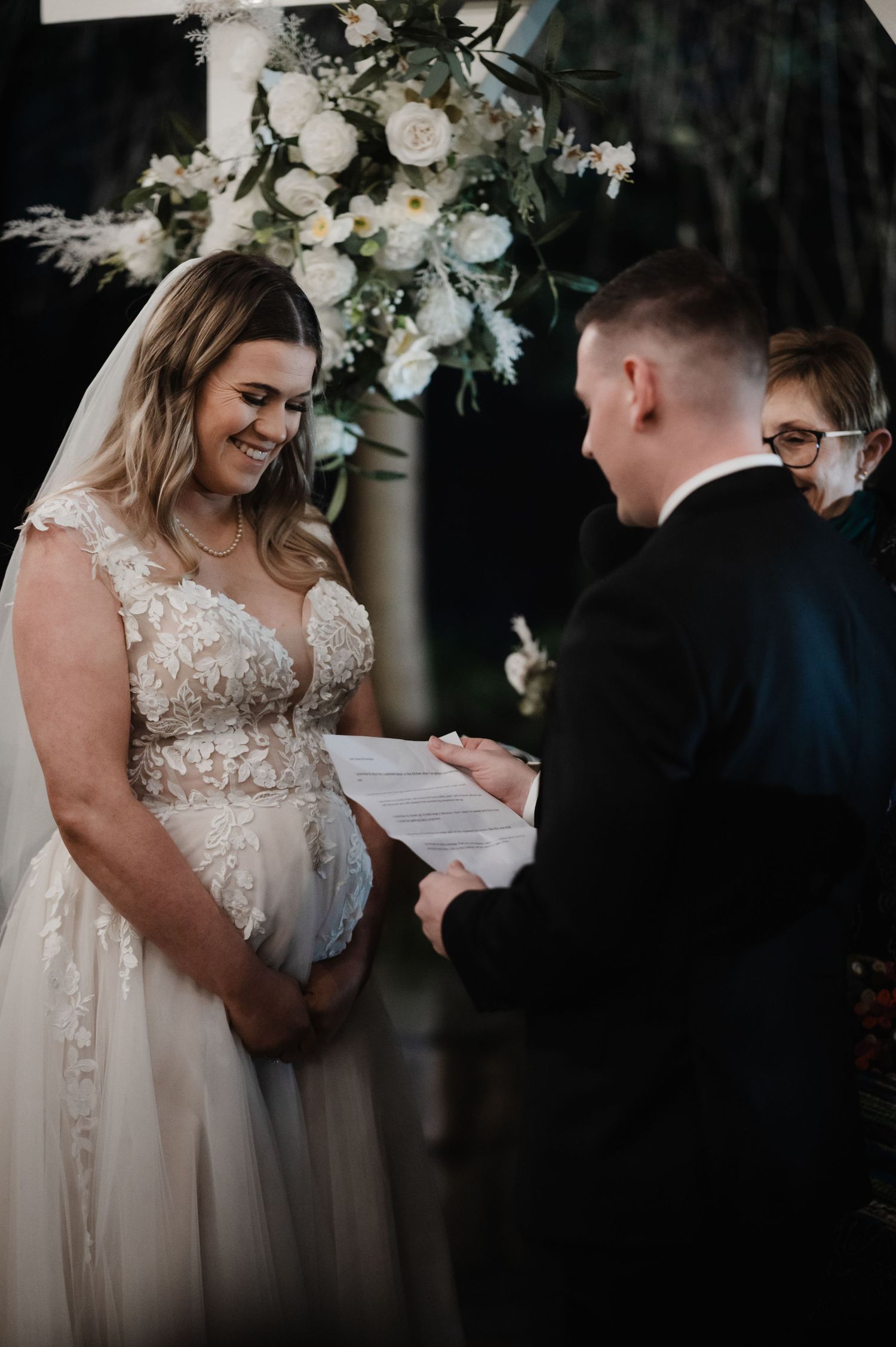 Intimate wedding ceremony moment with white floral arrangements overhead.