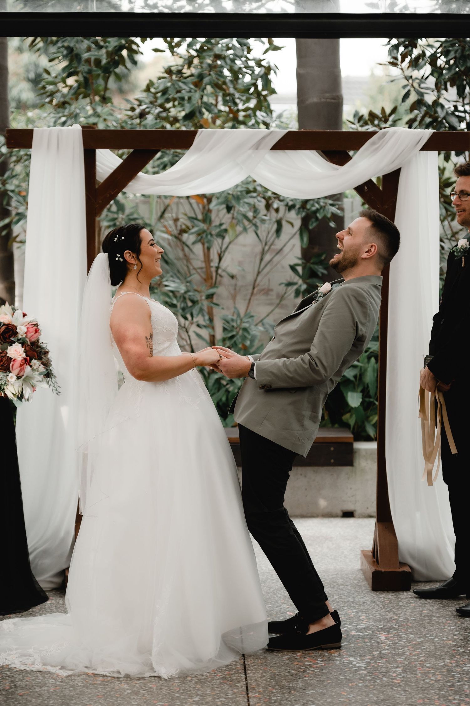 Wedding couple shares a playful dance moment under white drapes and garden surroundings.