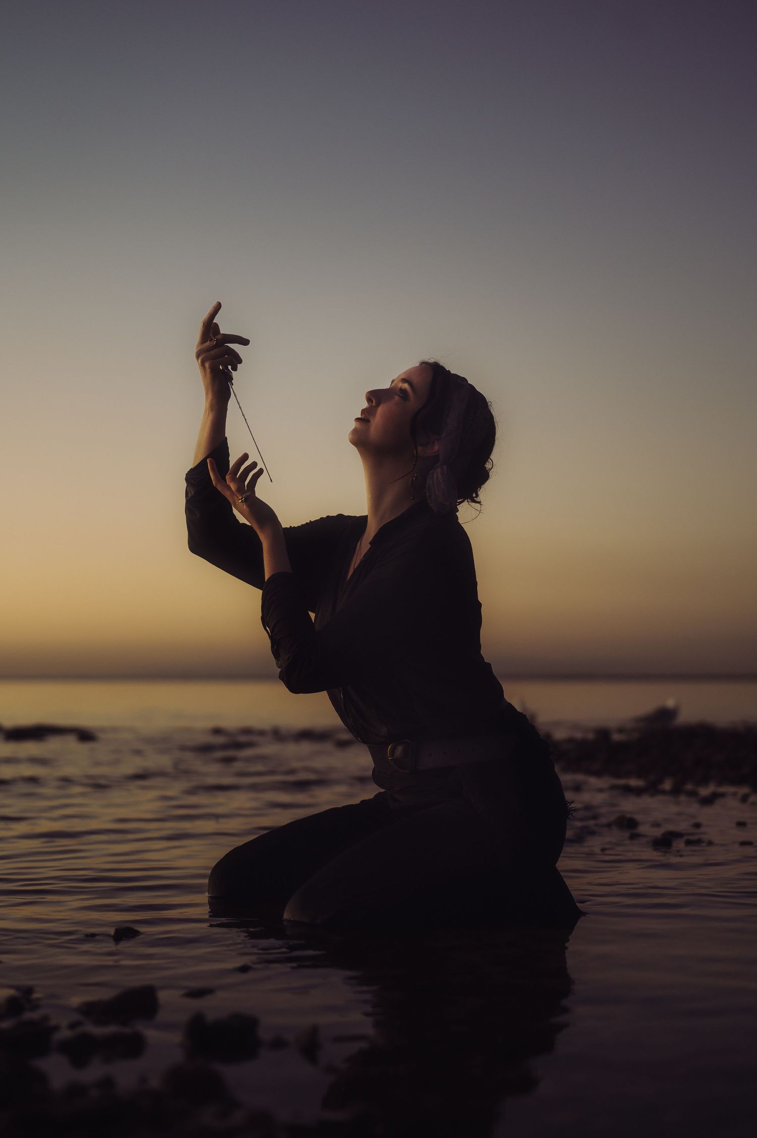Person poses dramatically against ocean horizon at sunset.