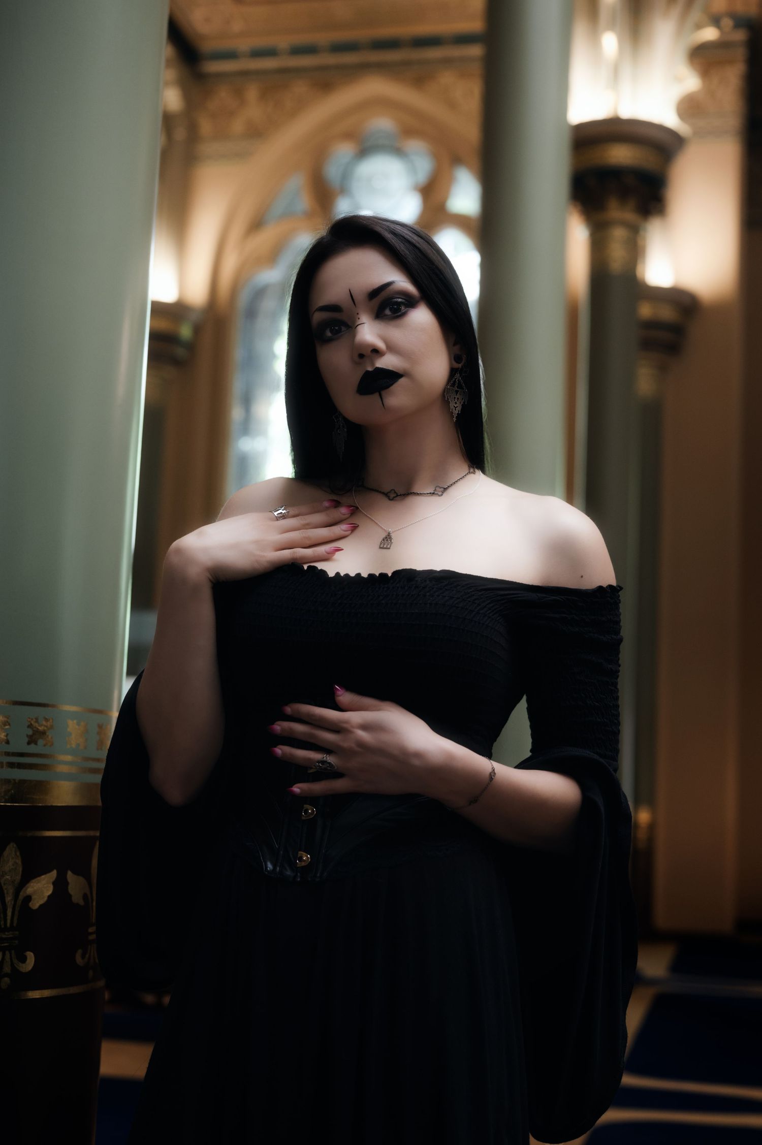 Moody portrait in black dress with dramatic makeup against architectural backdrop.