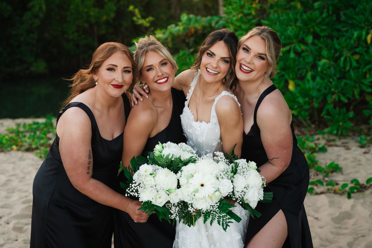 Bridesmaids in black dresses gather around white bouquet for group photo.