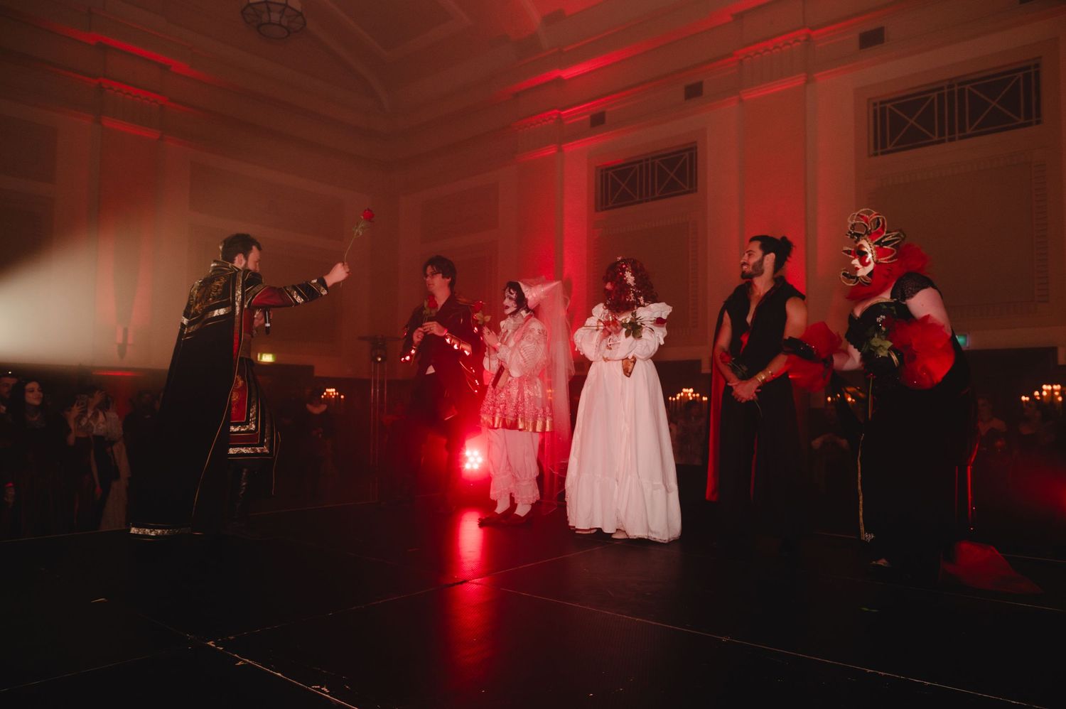 Costumed performers on stage bathed in dramatic red lighting during a theatrical Halloween event.