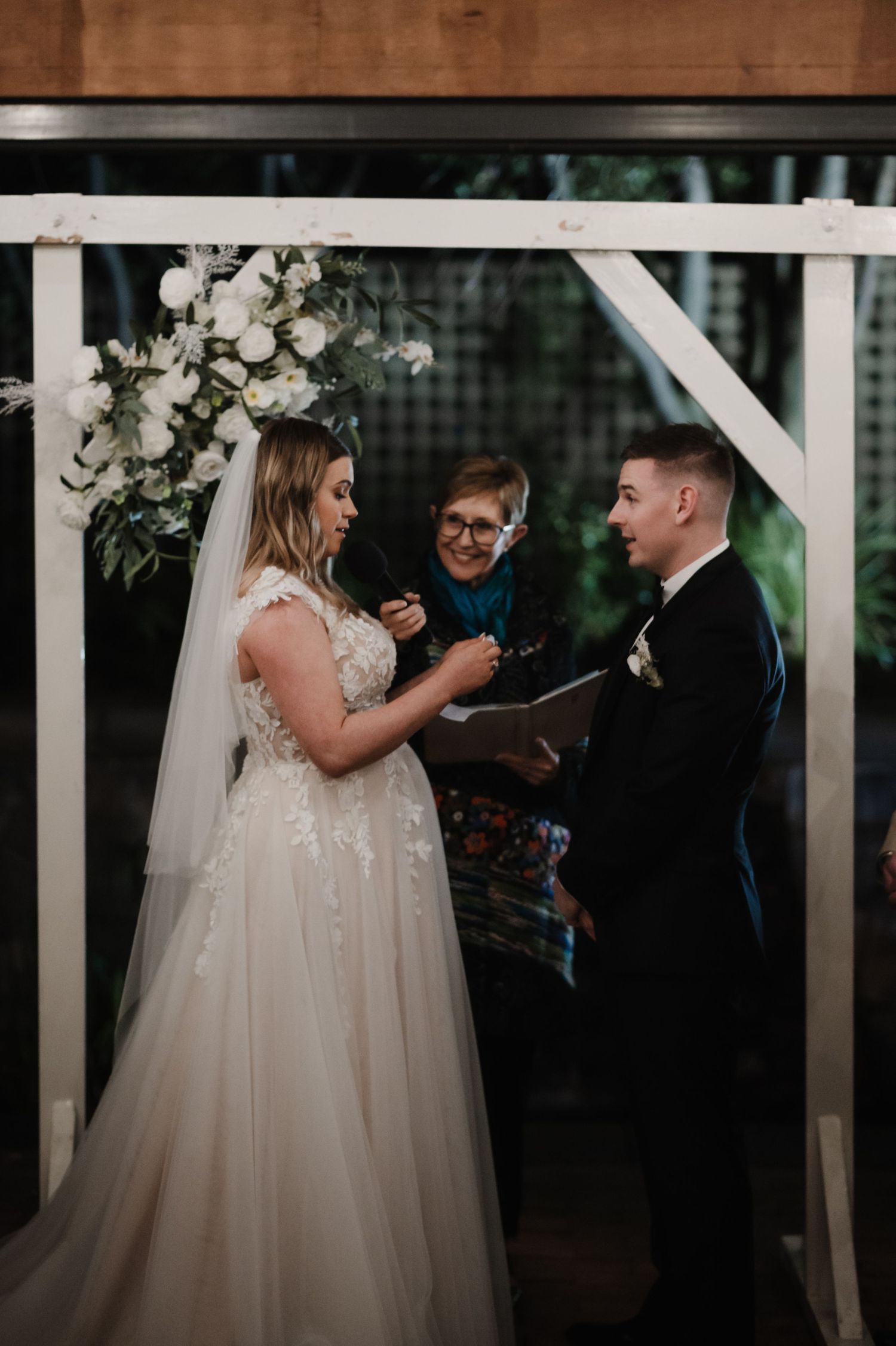 Wedding ceremony moment with couple exchanging vows under floral-decorated arch.