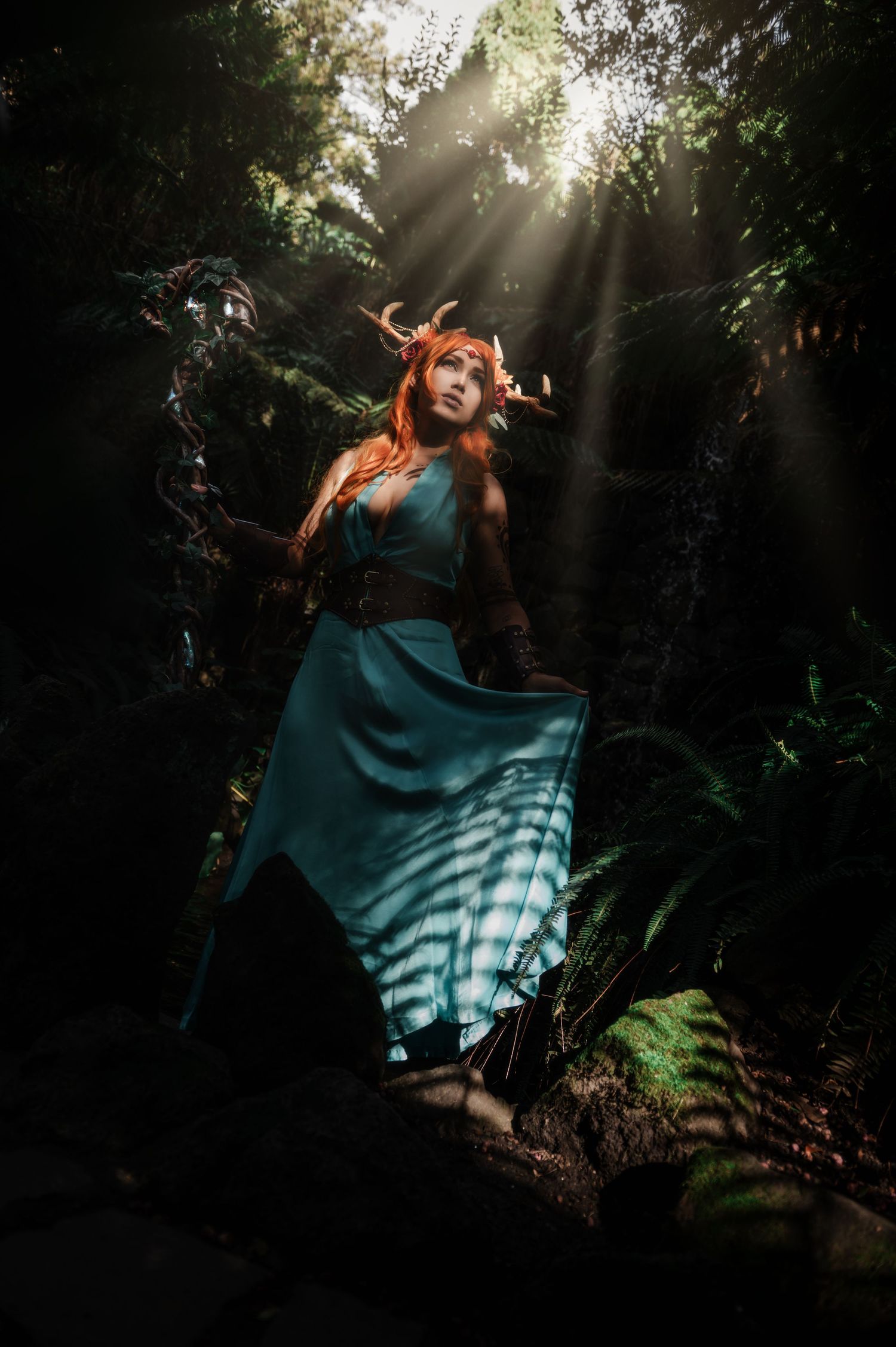 Ethereal forest photoshoot with a flowing teal dress and sunbeams streaming through trees.