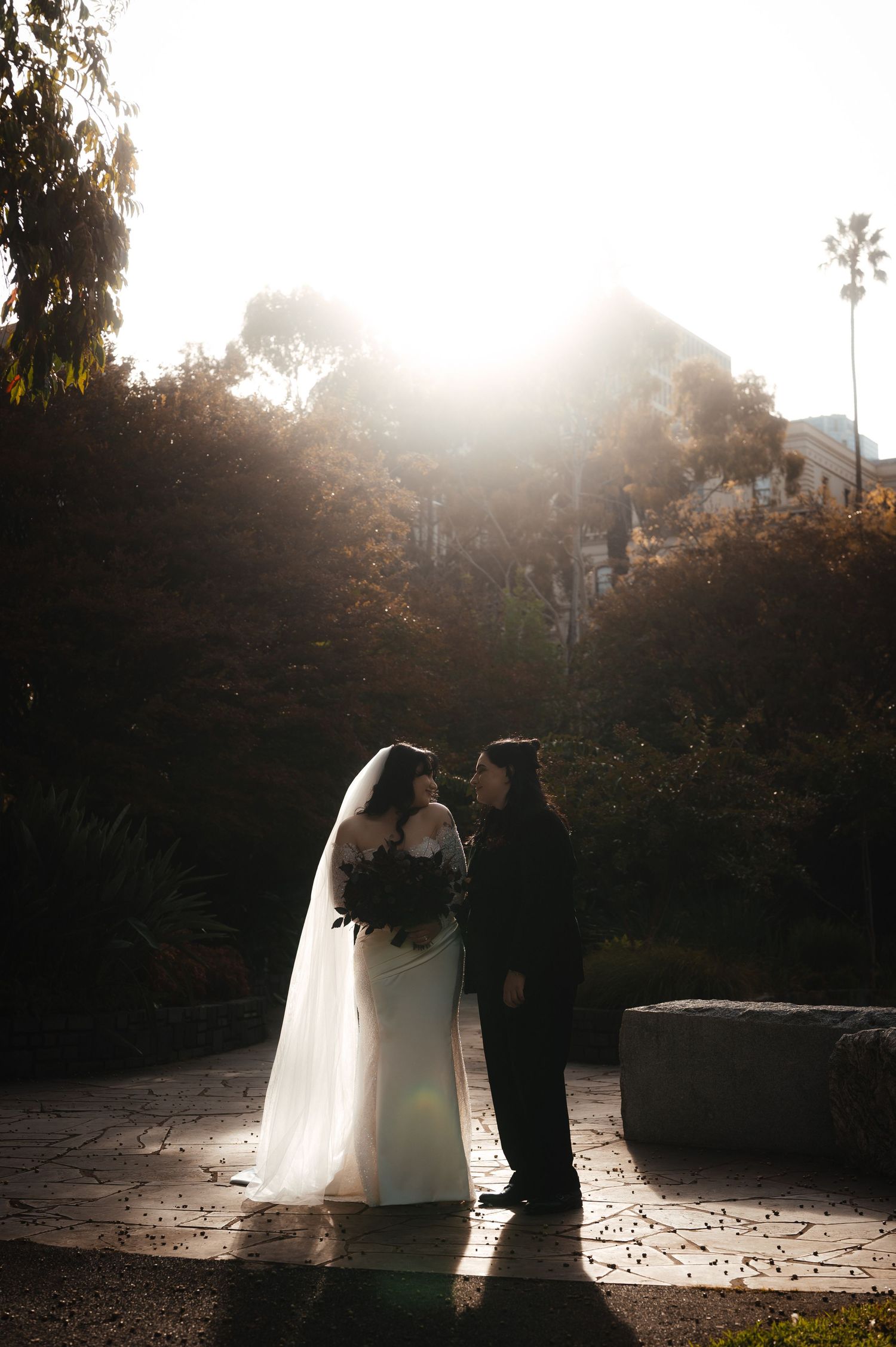 Sunlit wedding couple embracing on stone patio with dramatic backlighting.