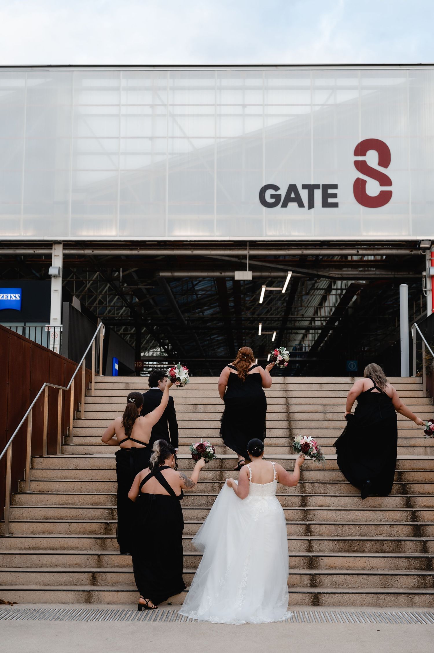 Wedding party members sit on concrete steps near Gate 3 entrance.