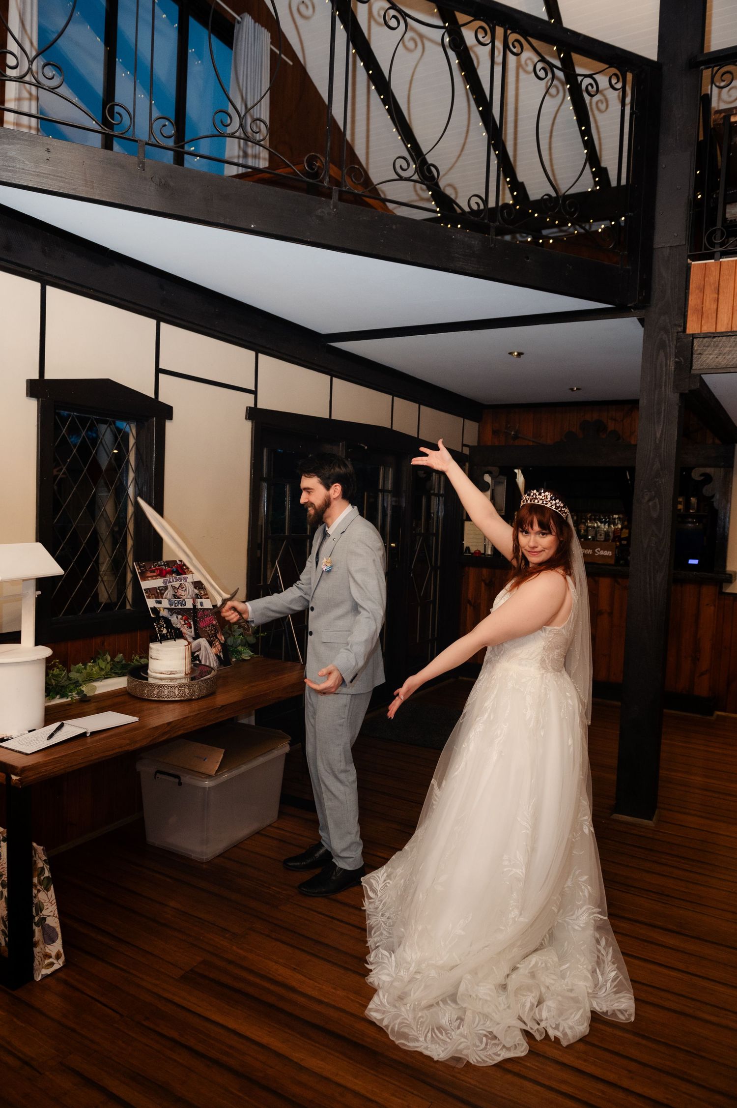 A couple dancing playfully at their wedding reception in a rustic venue with wooden floors and dark beams.