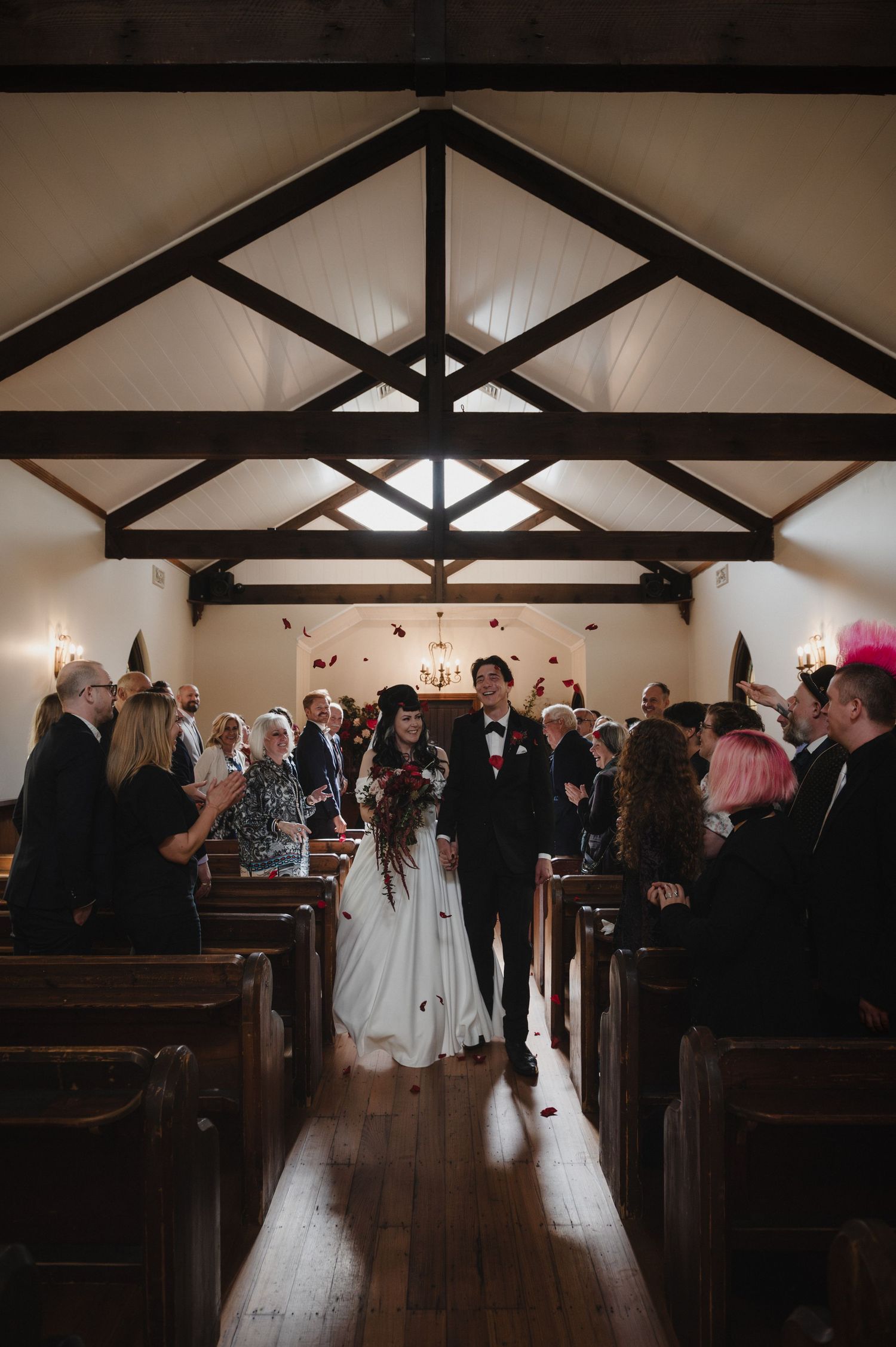 Wedding ceremony in progress inside a chapel with exposed wooden beams and natural lighting.