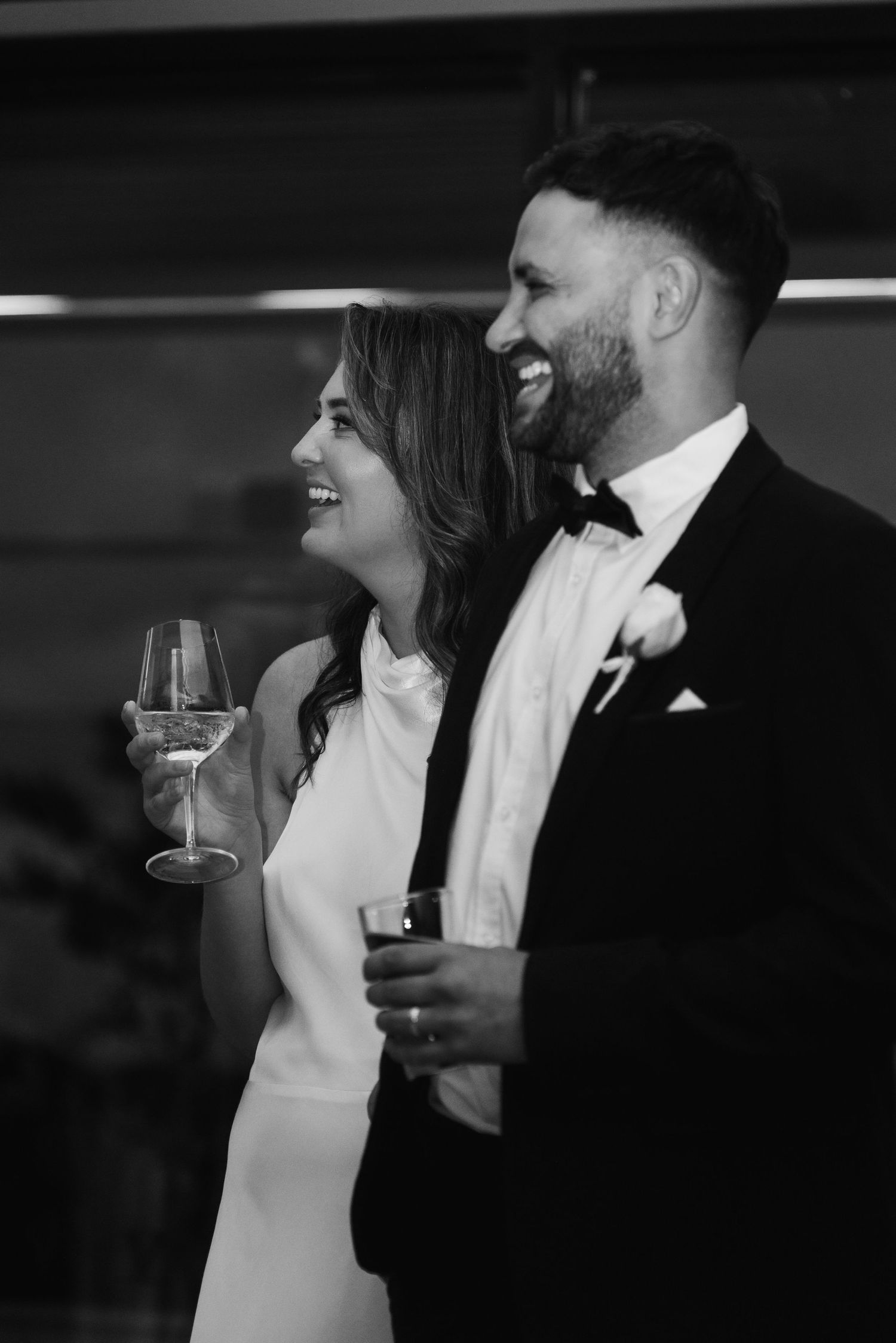 Black and white photo of couple sharing drinks and laughter at wedding reception.