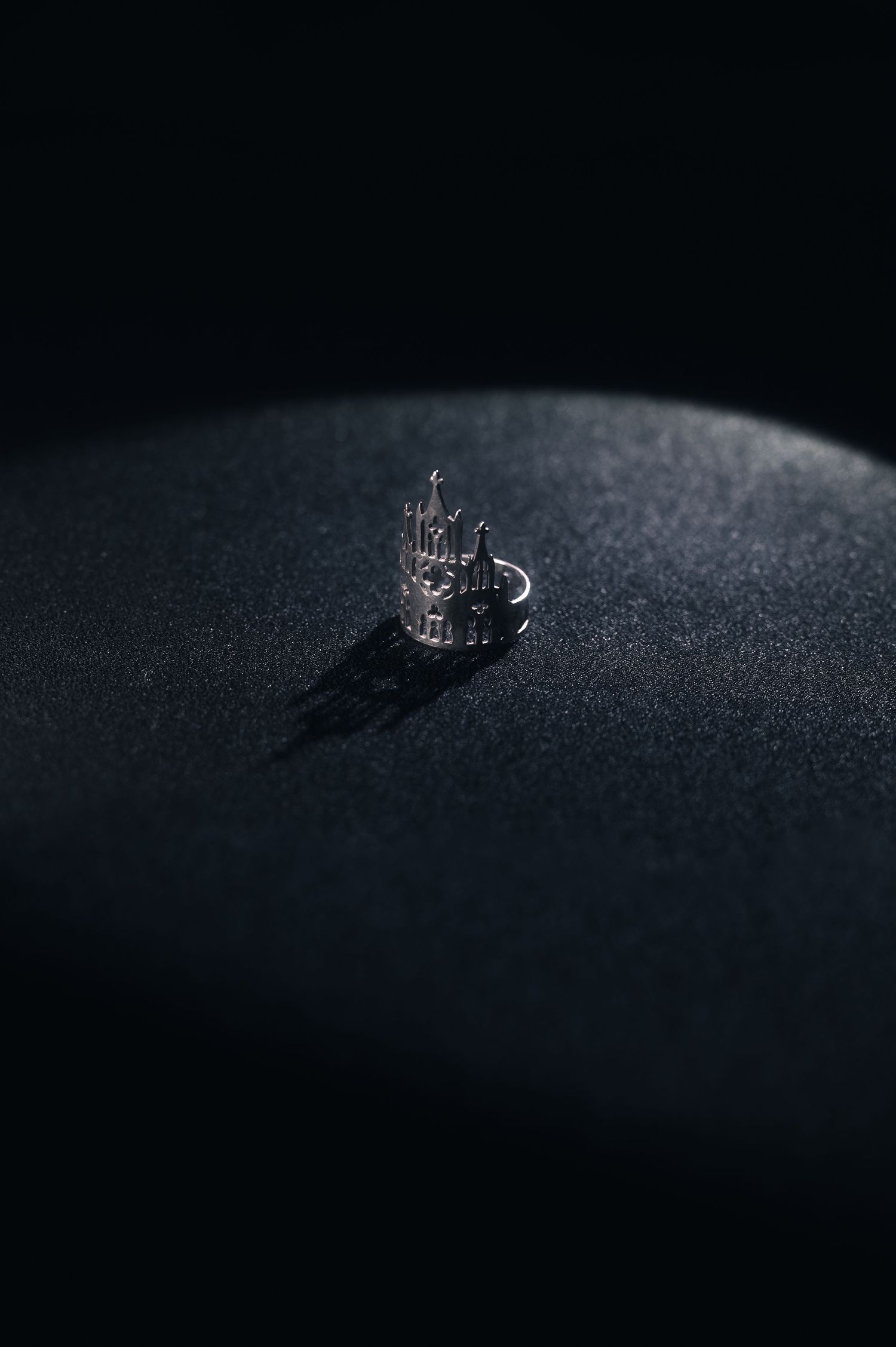 A detailed silver crown ring photographed on a dark textured surface.