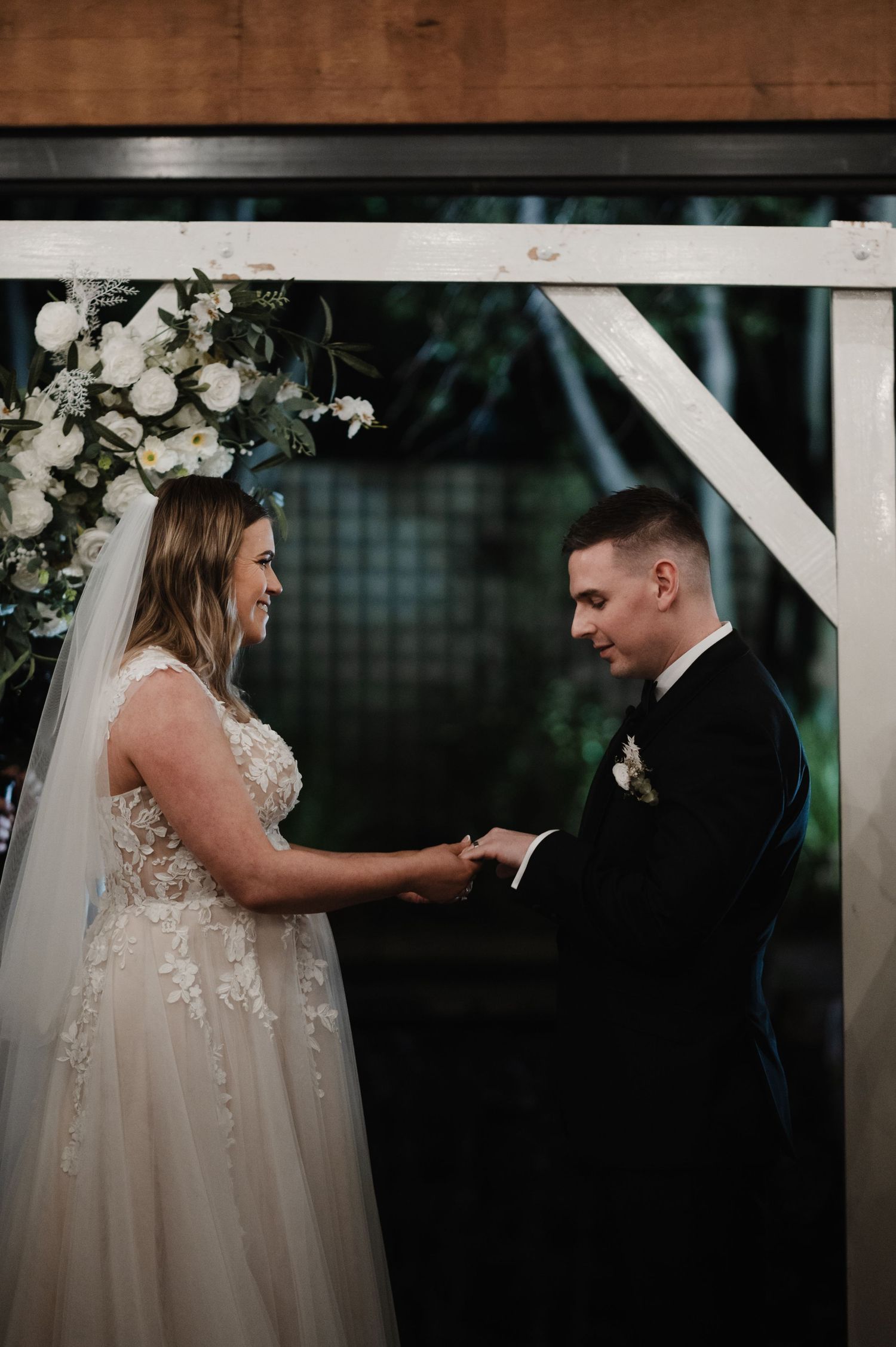 Wedding ceremony under white floral arch with romantic lighting.