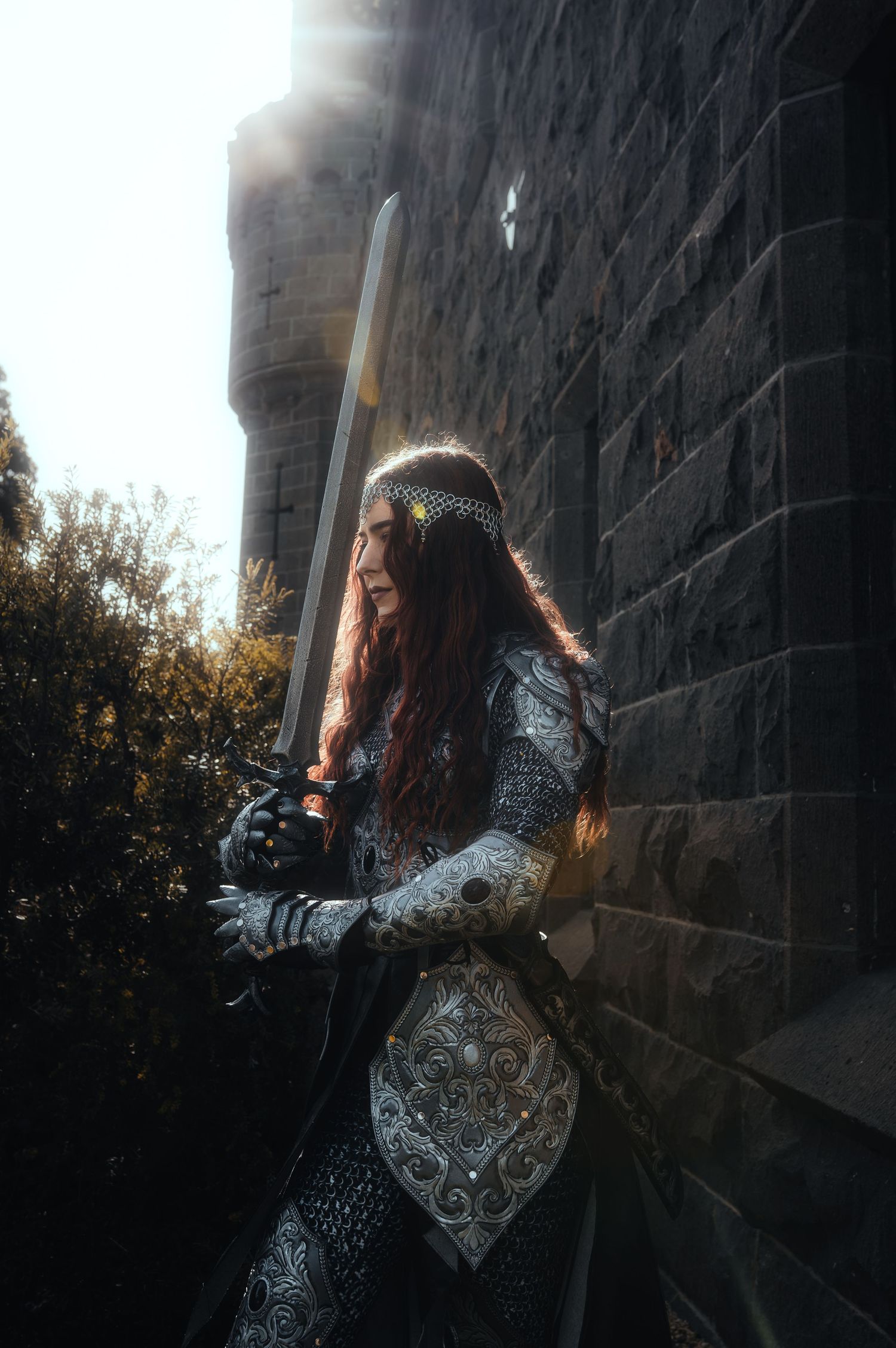 Warrior in silver etched armor wields sword near stone fortress wall.