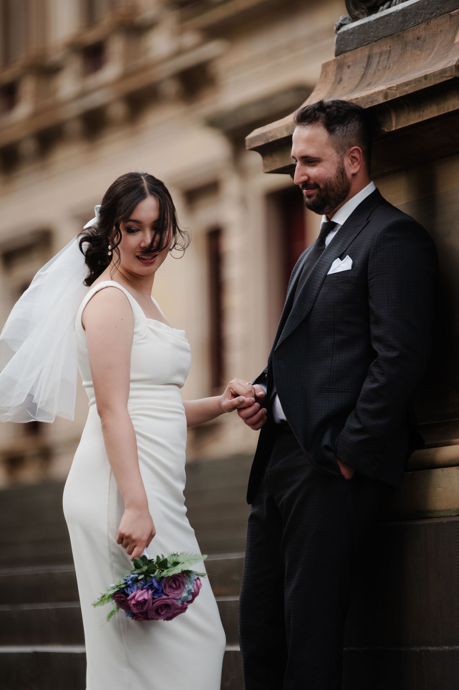 Bride and groom share tender moments along historic building exterior.