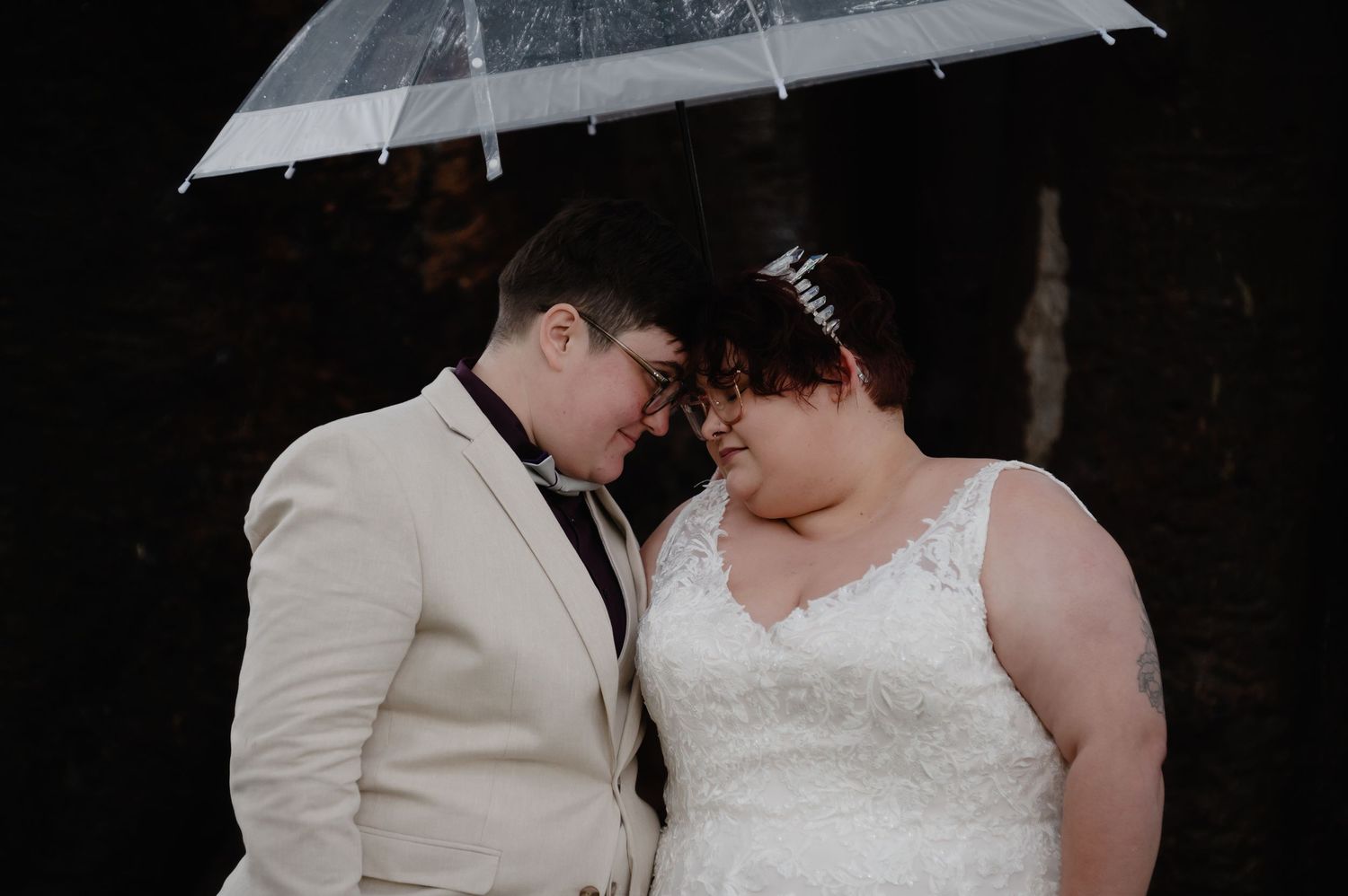 Couple sharing an intimate moment under a white umbrella during their wedding ceremony.