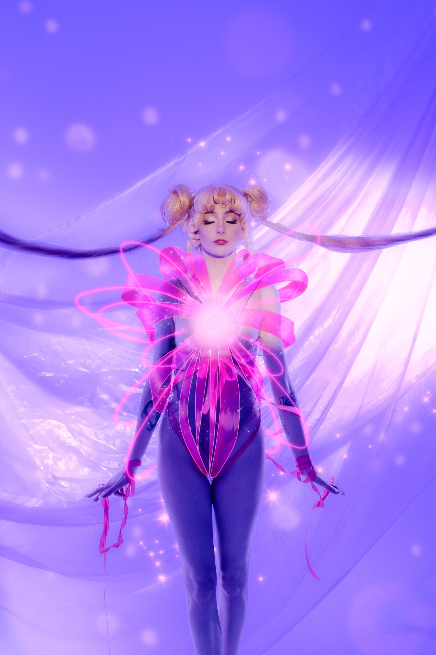 Cosplayer in purple bodysuit with glowing pink energy orb and flowing cape, resembling Sailor Moon character.