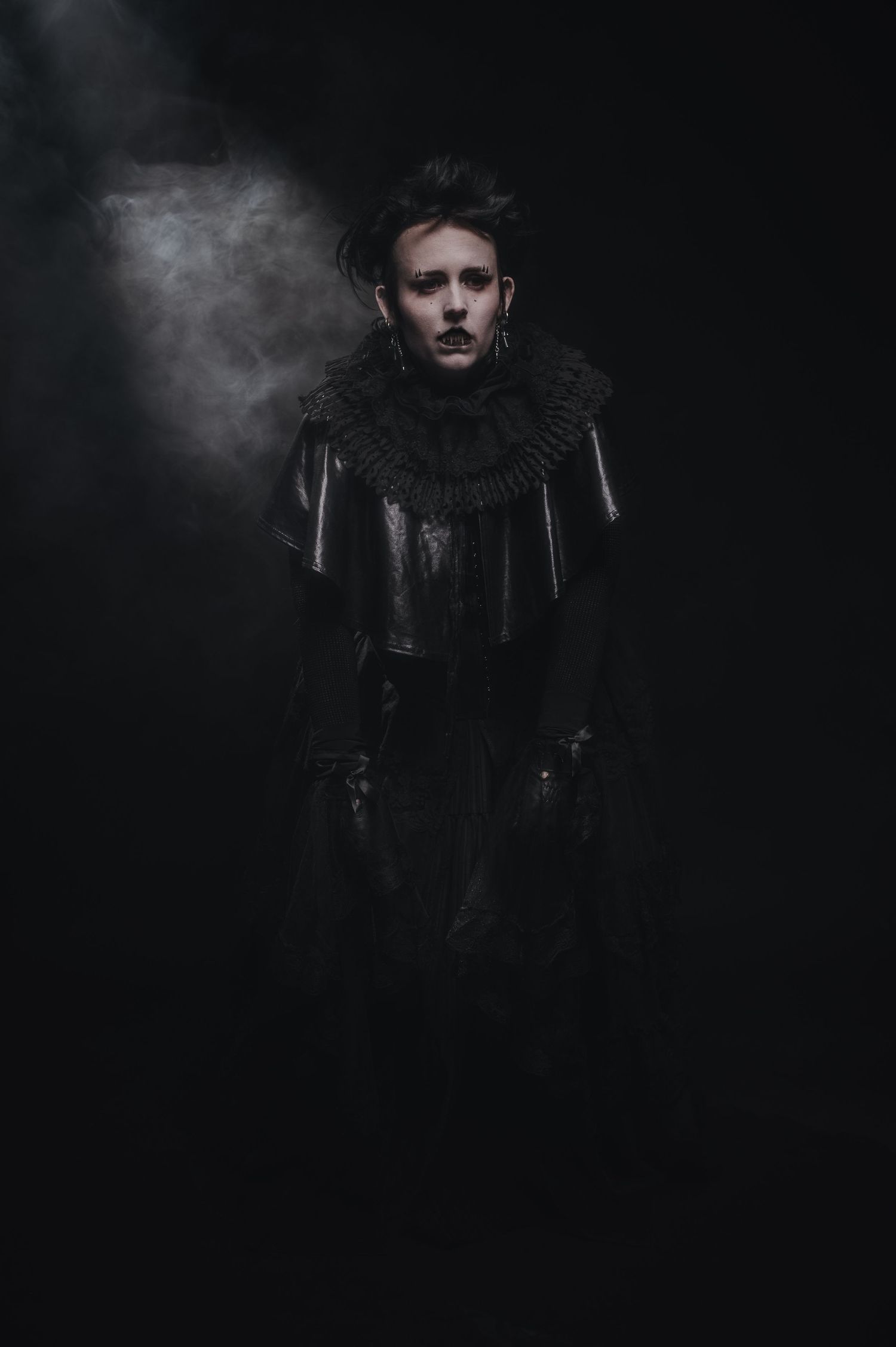Mysterious figure in dark clothing against smoky black background.