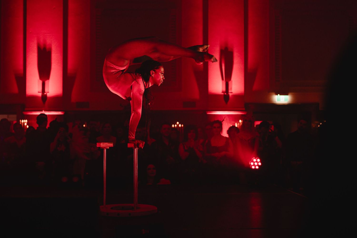 Acrobat performs a dramatic backbend on a pedestal under red lighting at an upscale evening event.