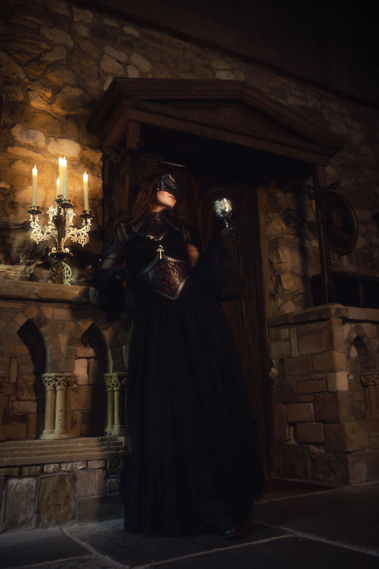 Dark gothic scene with candlelit stone walls and cloaked figures in shadow.