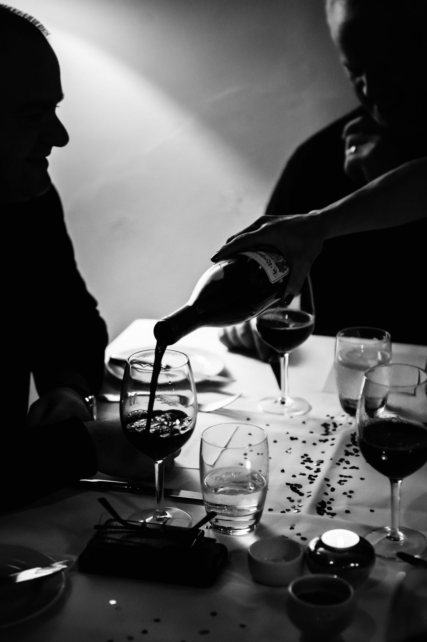Black and white photo of wine being poured at a dinner table with glasses and candles.
