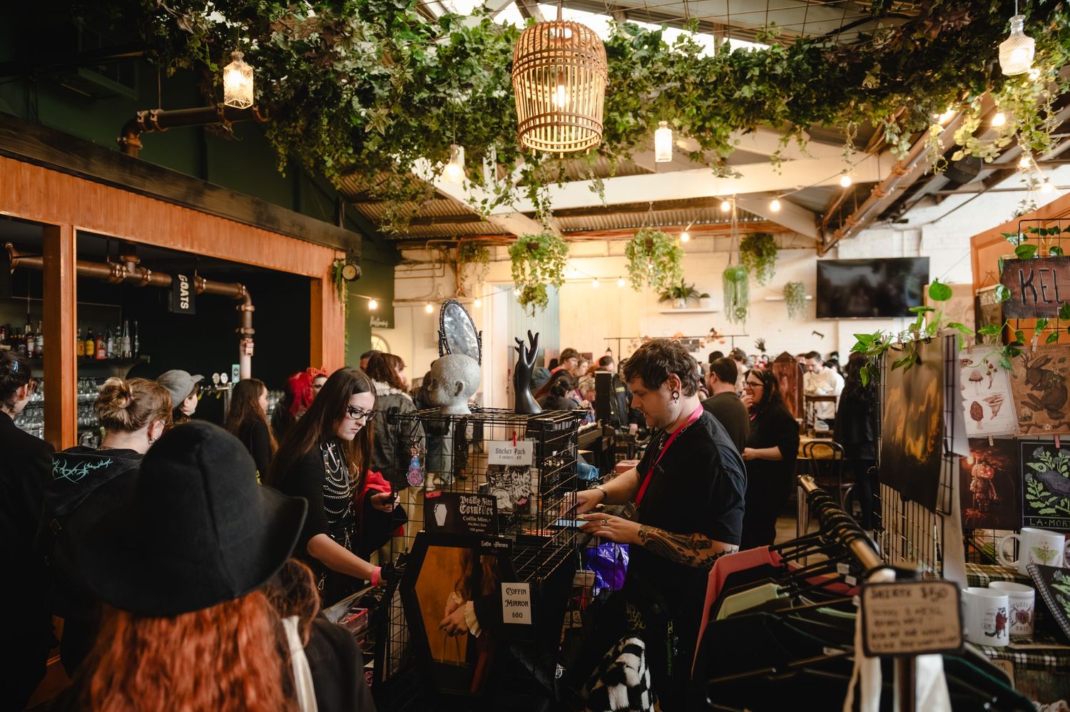 Busy bar interior with lush greenery, warm lighting, and patrons enjoying drinks in a vibrant social setting.
