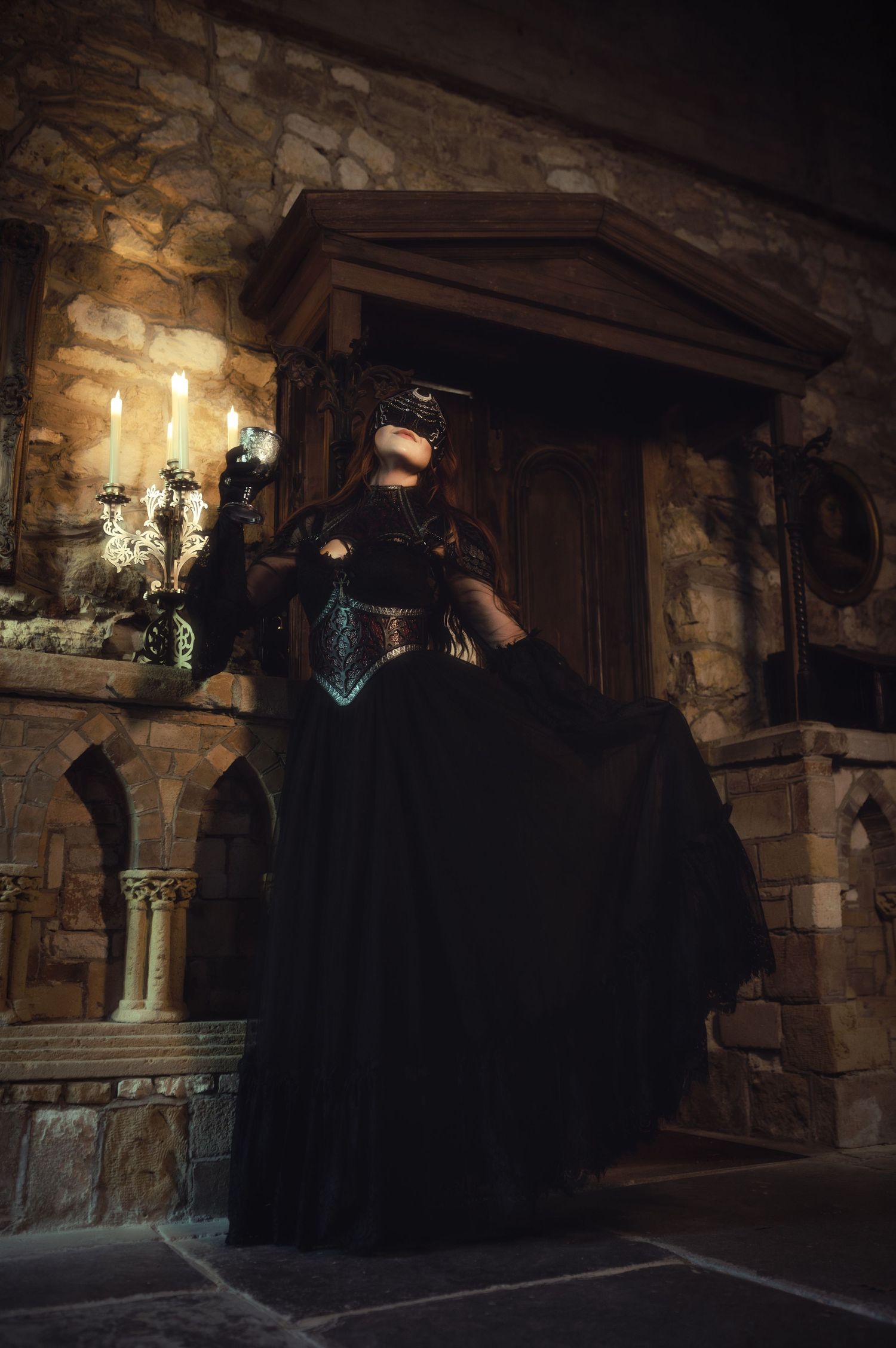 A dramatic gothic costume with flowing black dress photographed in a stone castle setting.