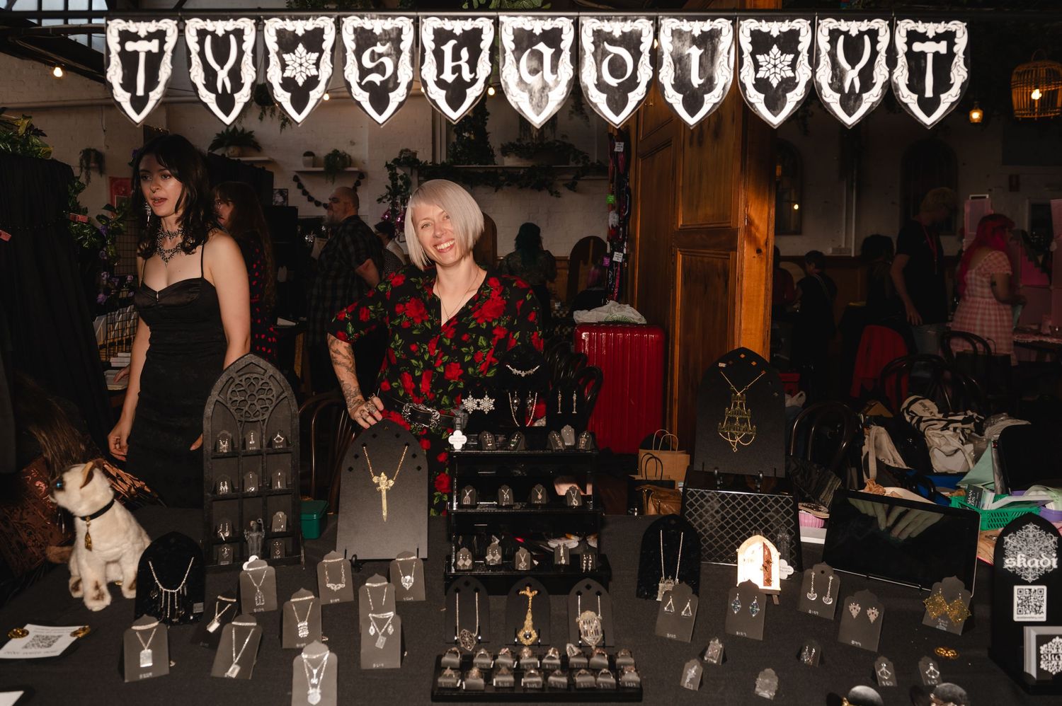 People gather at a dimly lit event venue with tables and chairs arranged for a social function.