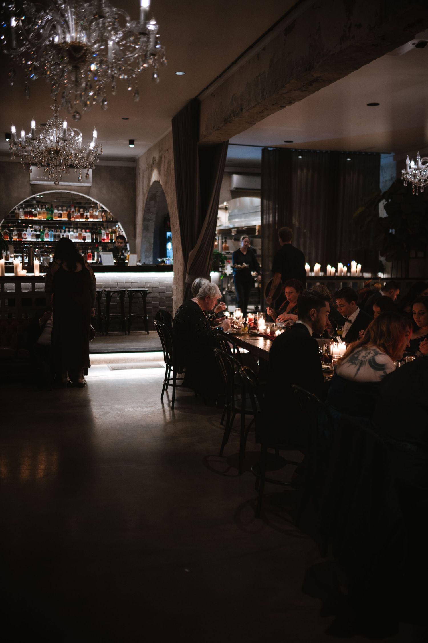 Dark and moody reception venue with crystal chandeliers and dining tables.